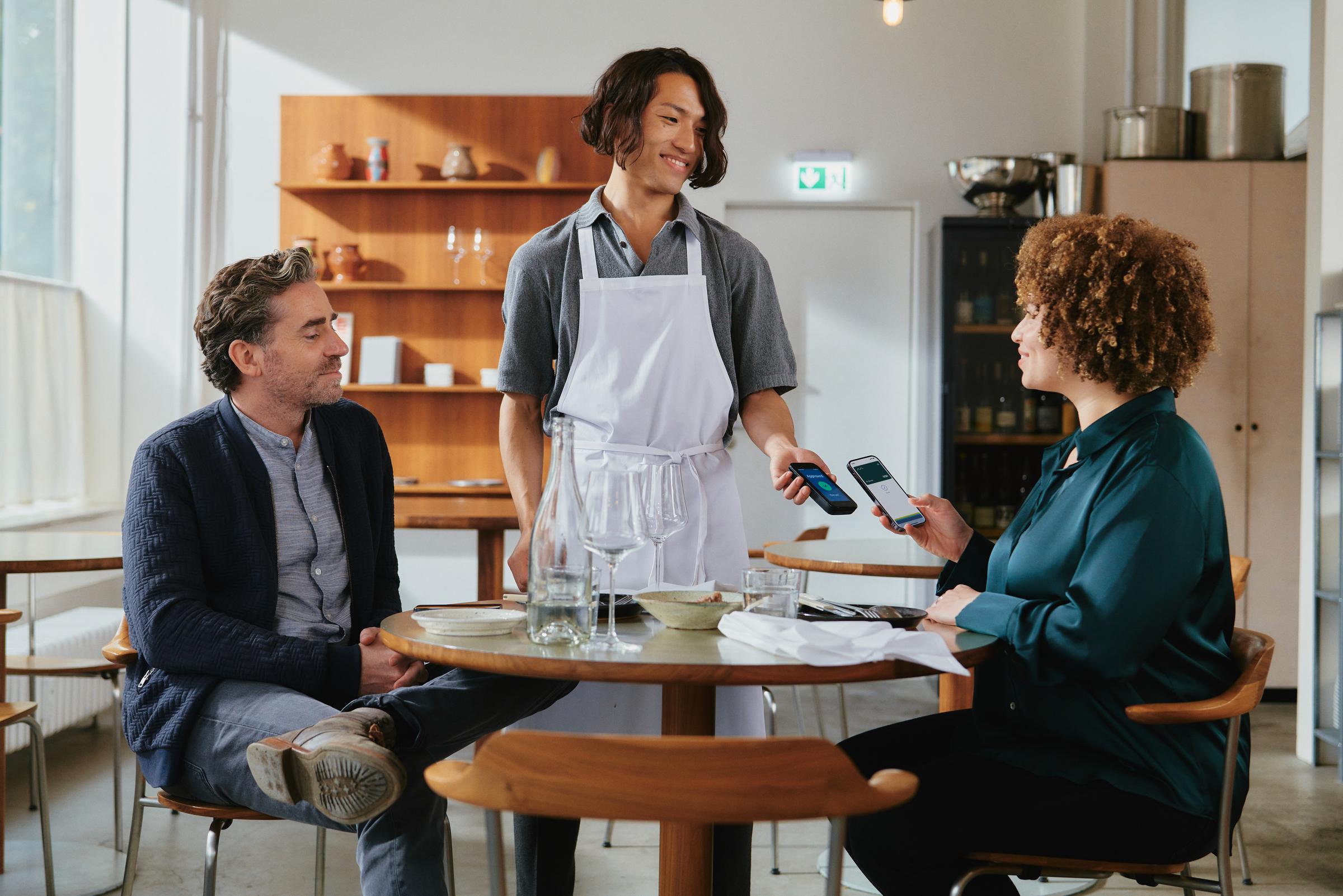 A couple in a restaurant paying for food by tapping a smartphone on Adyen's AMS1 terminal.