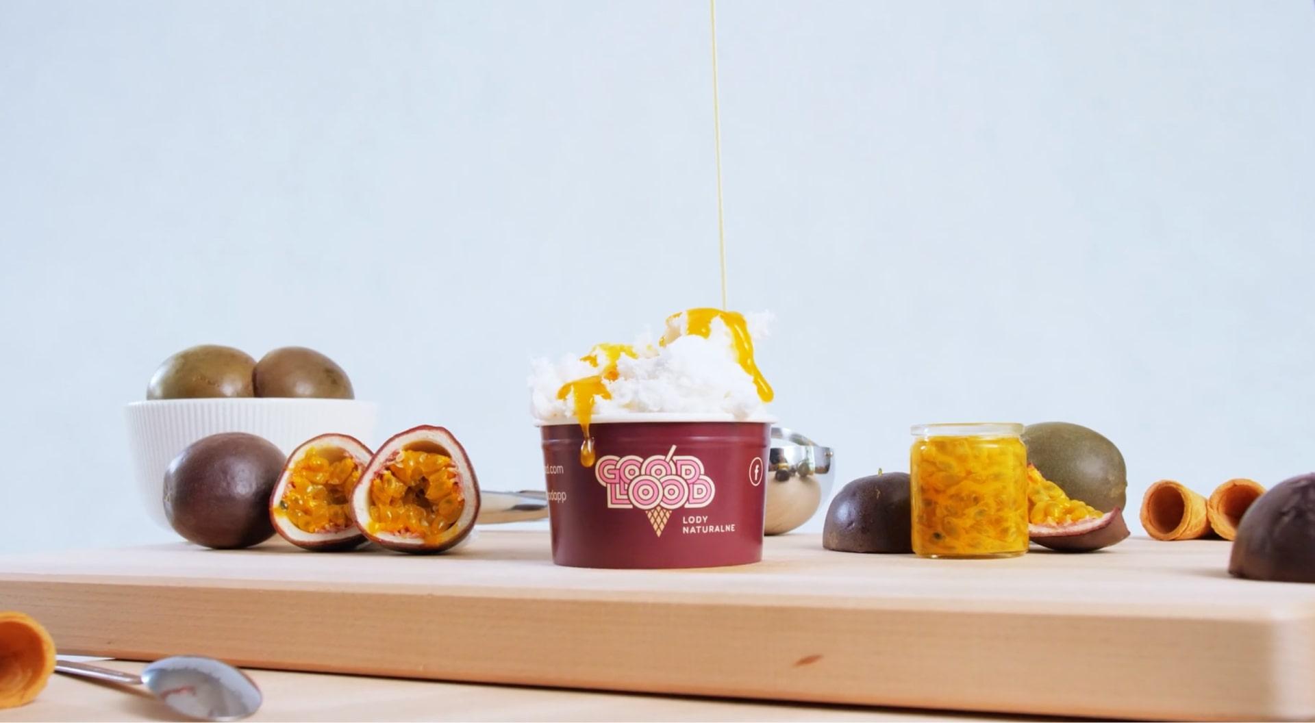 Kubek lodu Good Lood na drewnianej desce z owocem pasji i dodatkami.