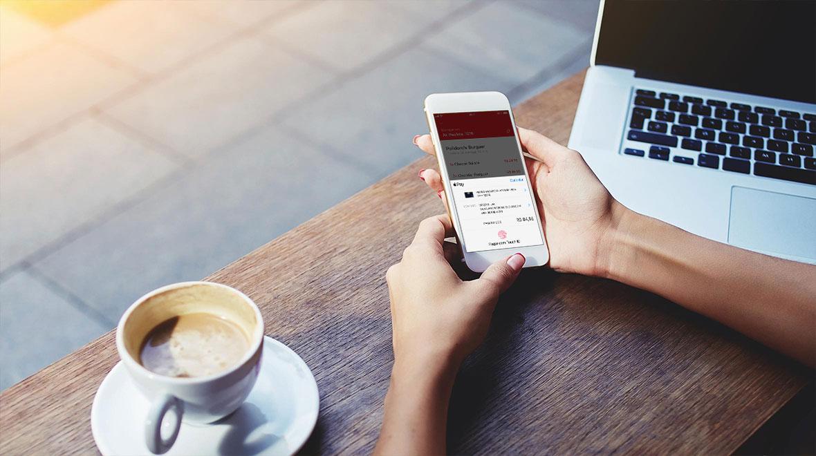 Persona que sostiene un smartphone con la interfaz de pago de Adyen, al lado de una taza de café y una laptop.