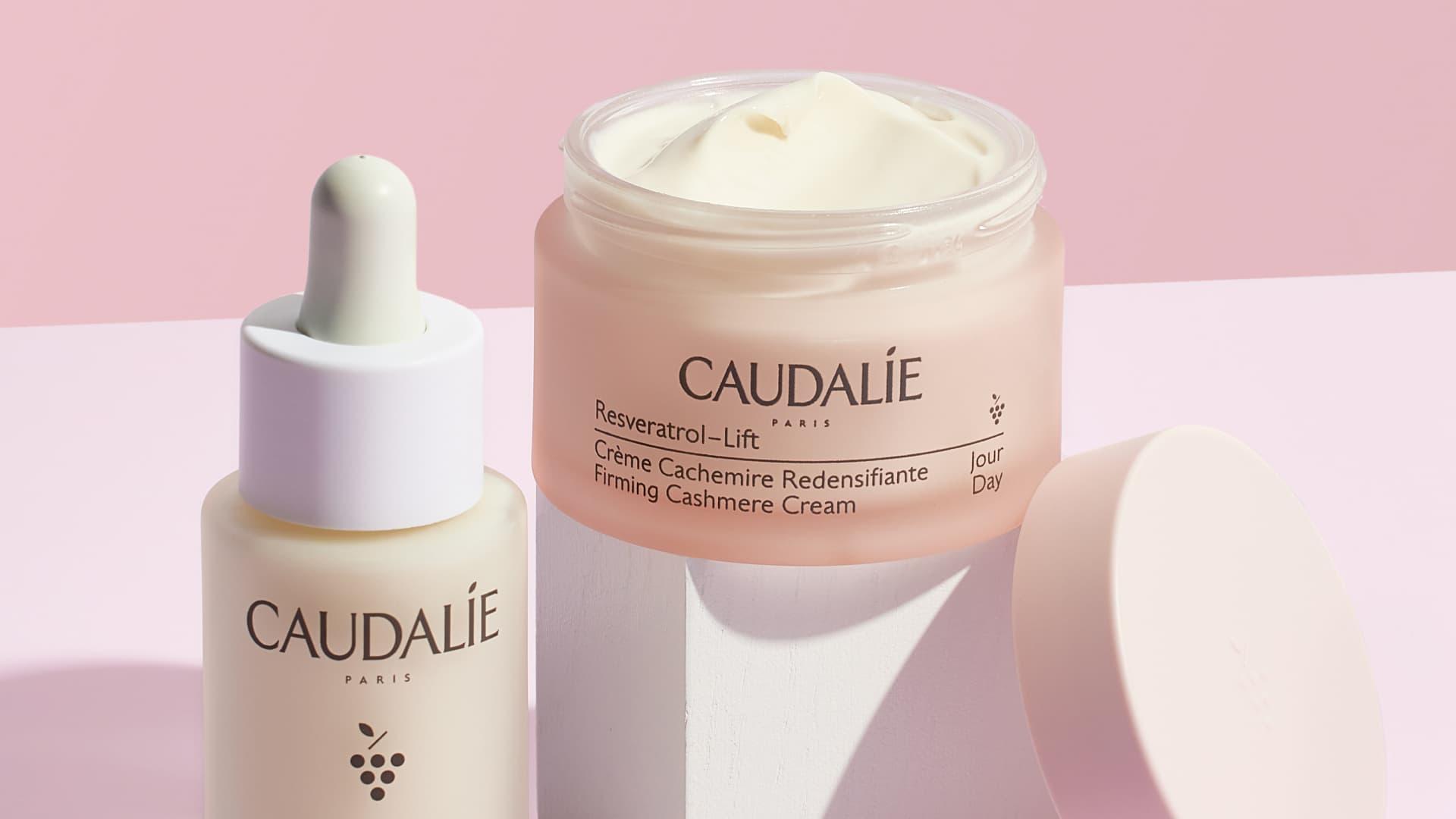 Prodotti per la cura della pelle Caudalie con vasetto di crema e flacone con contagocce su sfondo rosa