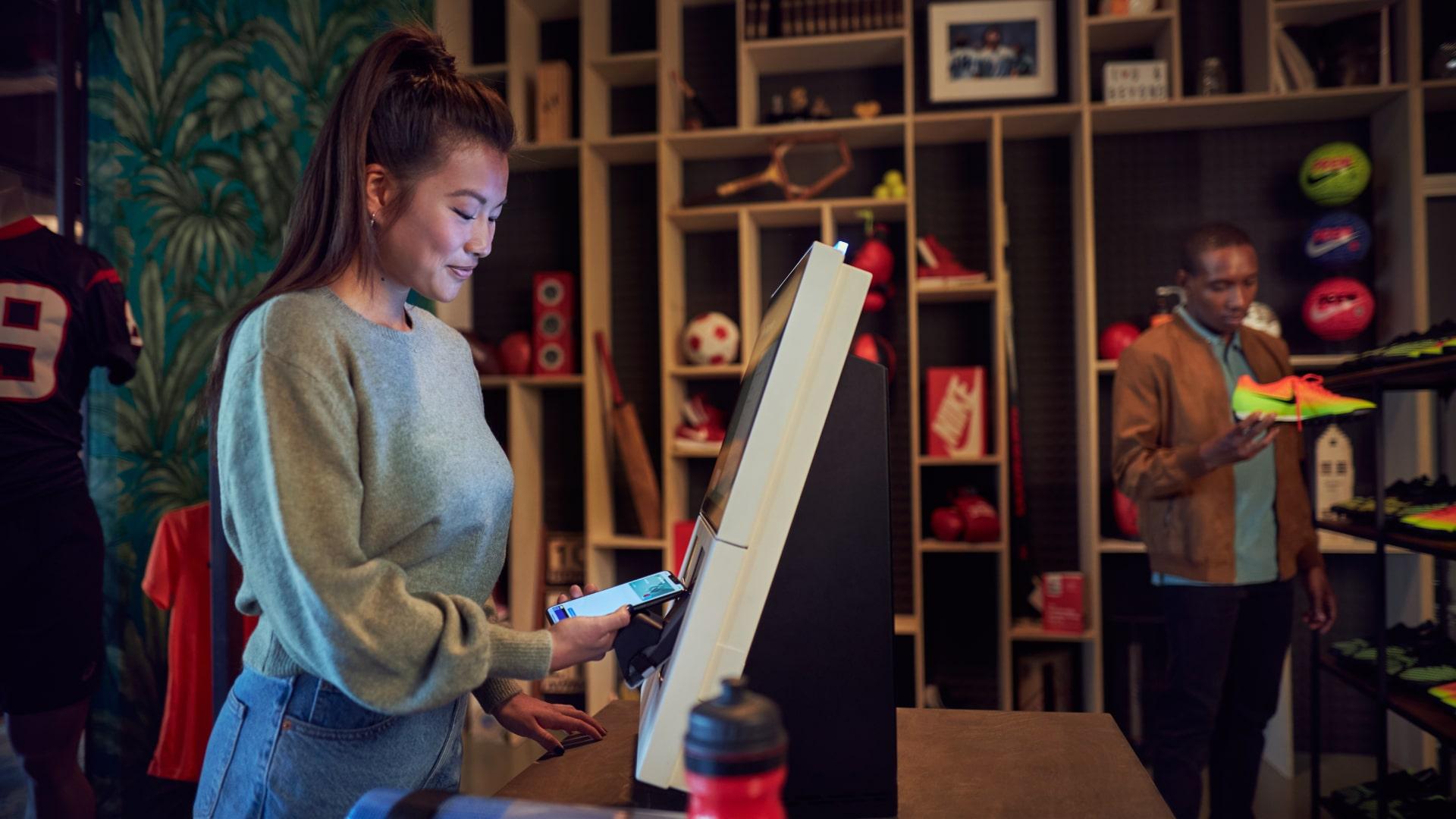 Mujer utilizando su teléfono para una transacción en un terminal de pago Adyen en una tienda de deportes.