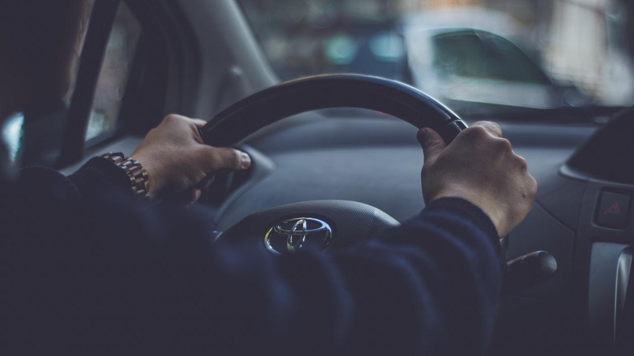 Vue rapprochée des mains d'une personne sur un volant avec un écusson Toyota.