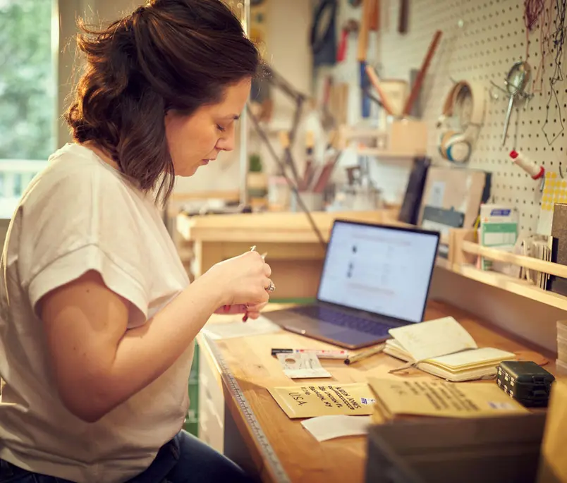 Person handcrafting jewelry at a workbench with a laptop displaying Adyen's checkout UI.