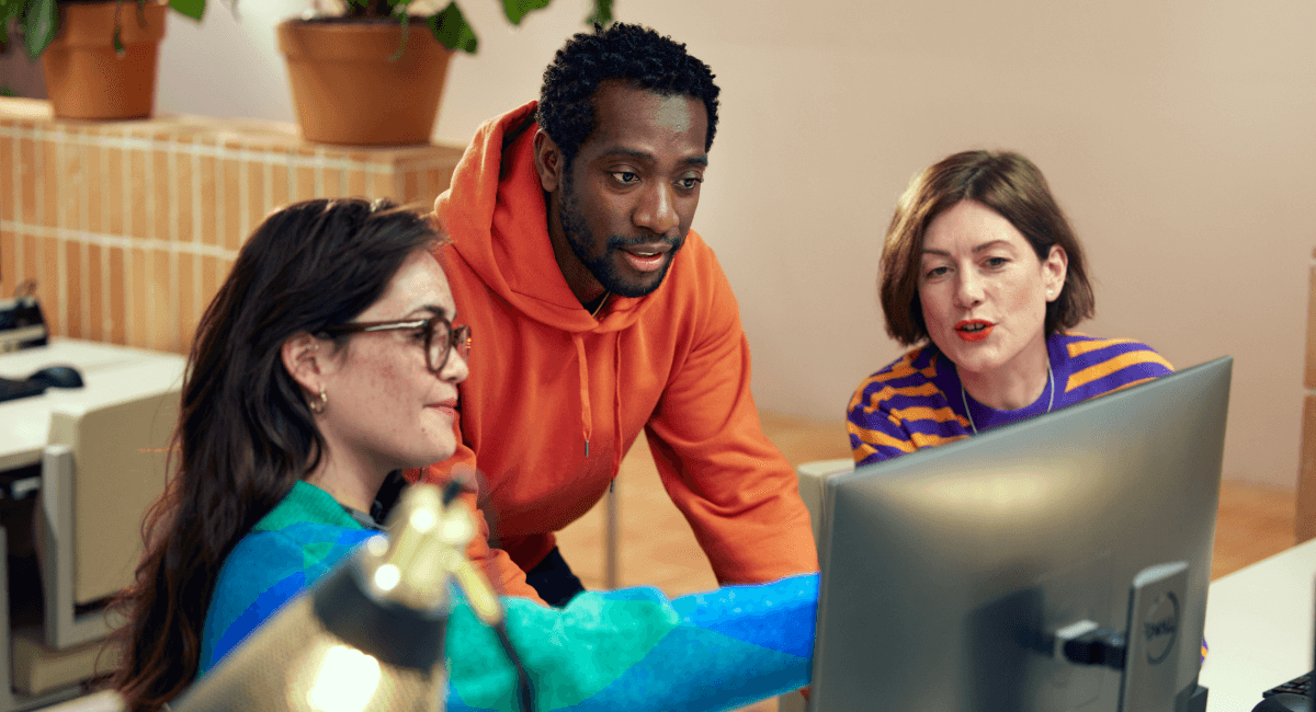 Três colegas de trabalho colaborando no computador em um escritório moderno.