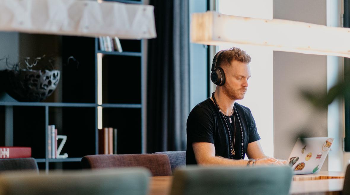 Focused individual working on a laptop with headphones in a modern office setting.