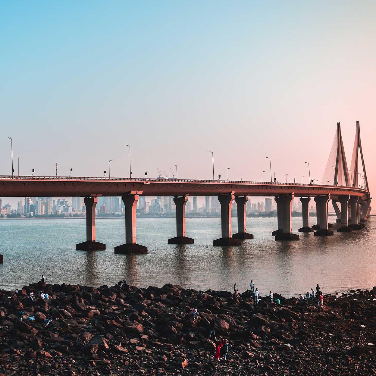 Solnedgangsutsikt over en hengebro over et vann med byens skyline i bakgrunnen