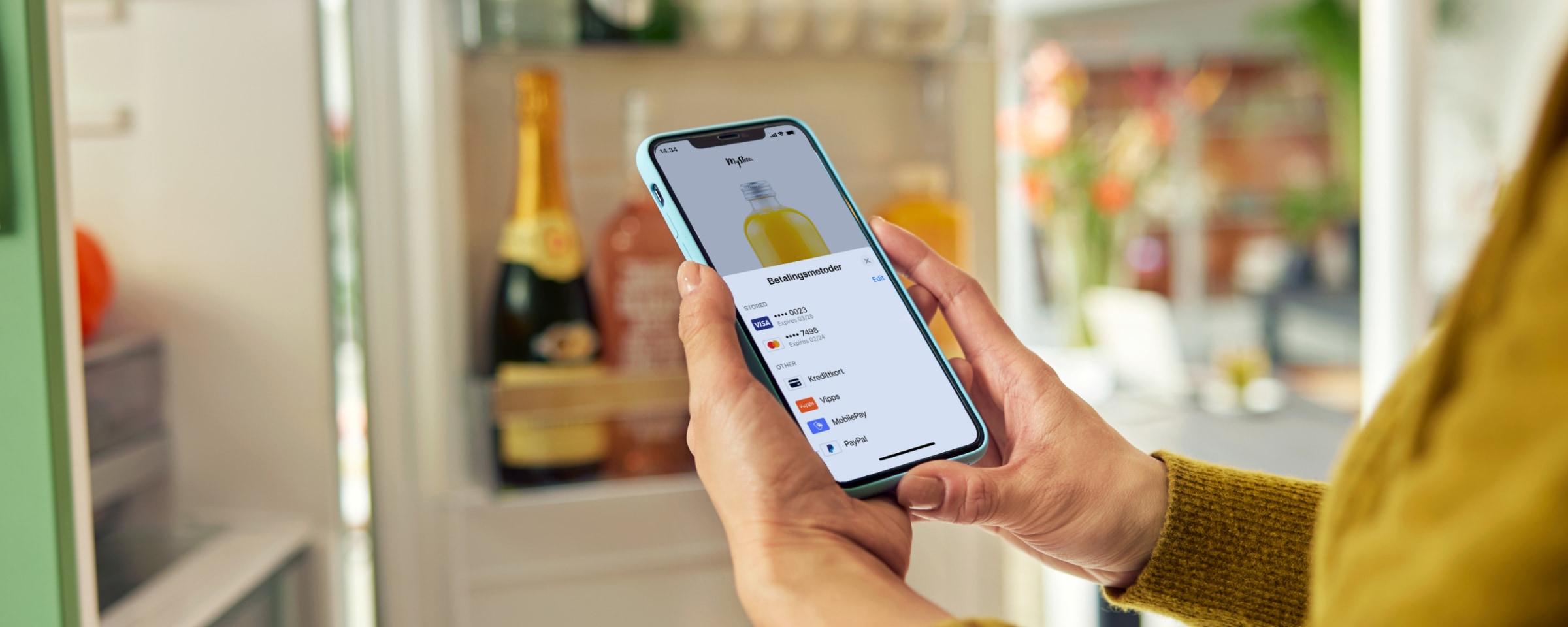 Nærbilde av en persons hender som holder en smartphone med Adyens betalingsapp-grunnflate på skjermen