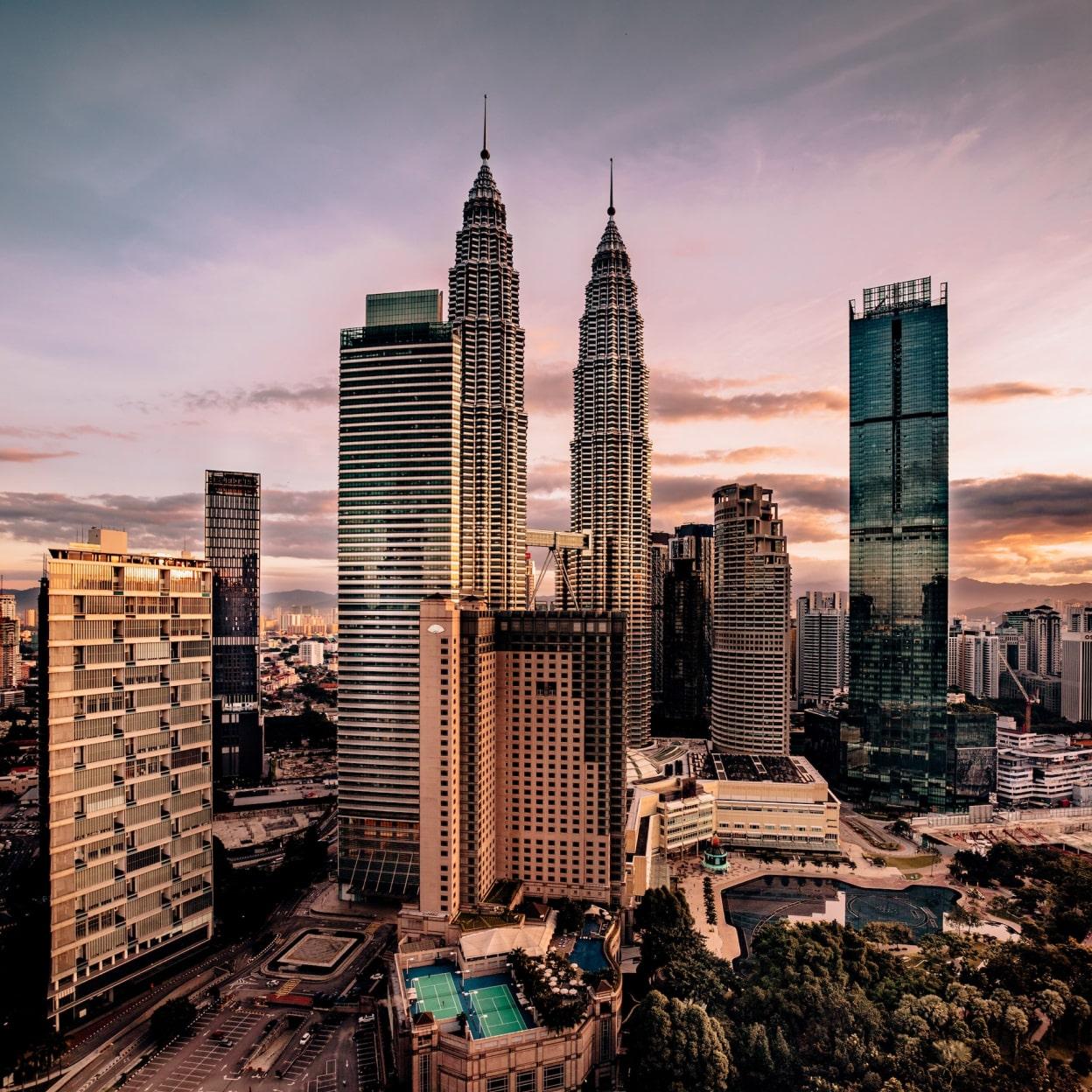Puesta de sol dramática sobre un paisaje urbano con torres gemelas icónicas y rascacielos modernos.