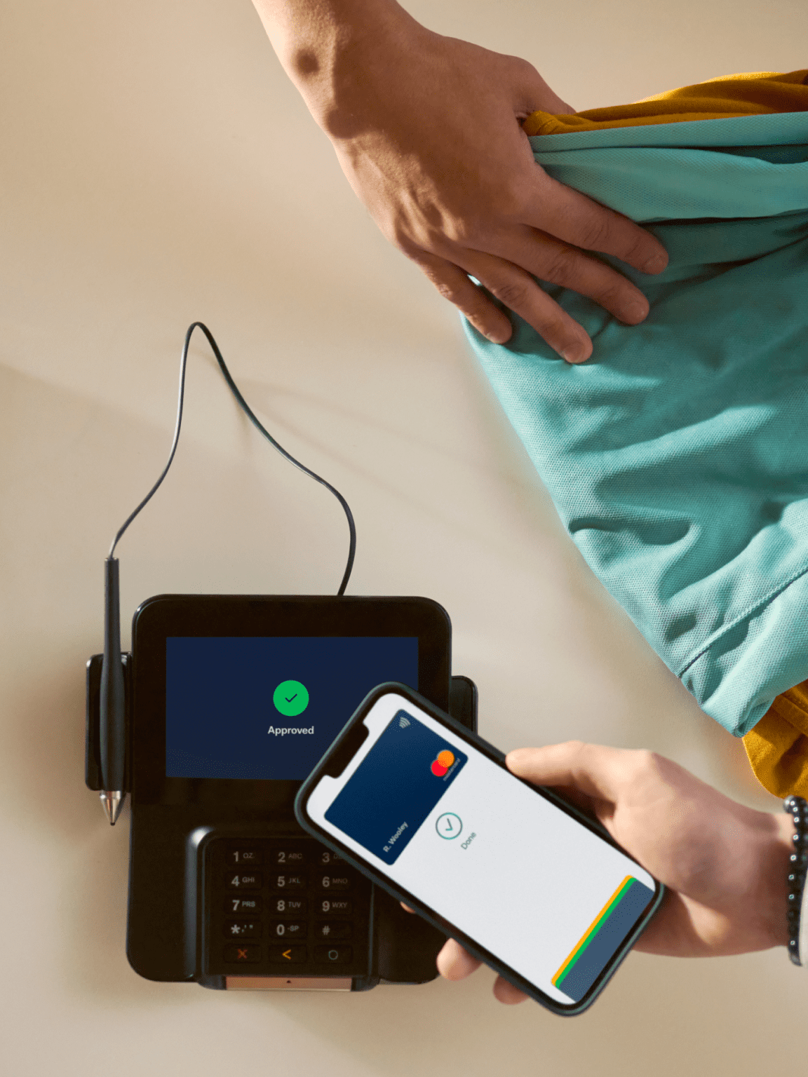 Person using a smartphone to complete a contactless payment on an Adyen terminal indicating 'Approved'.