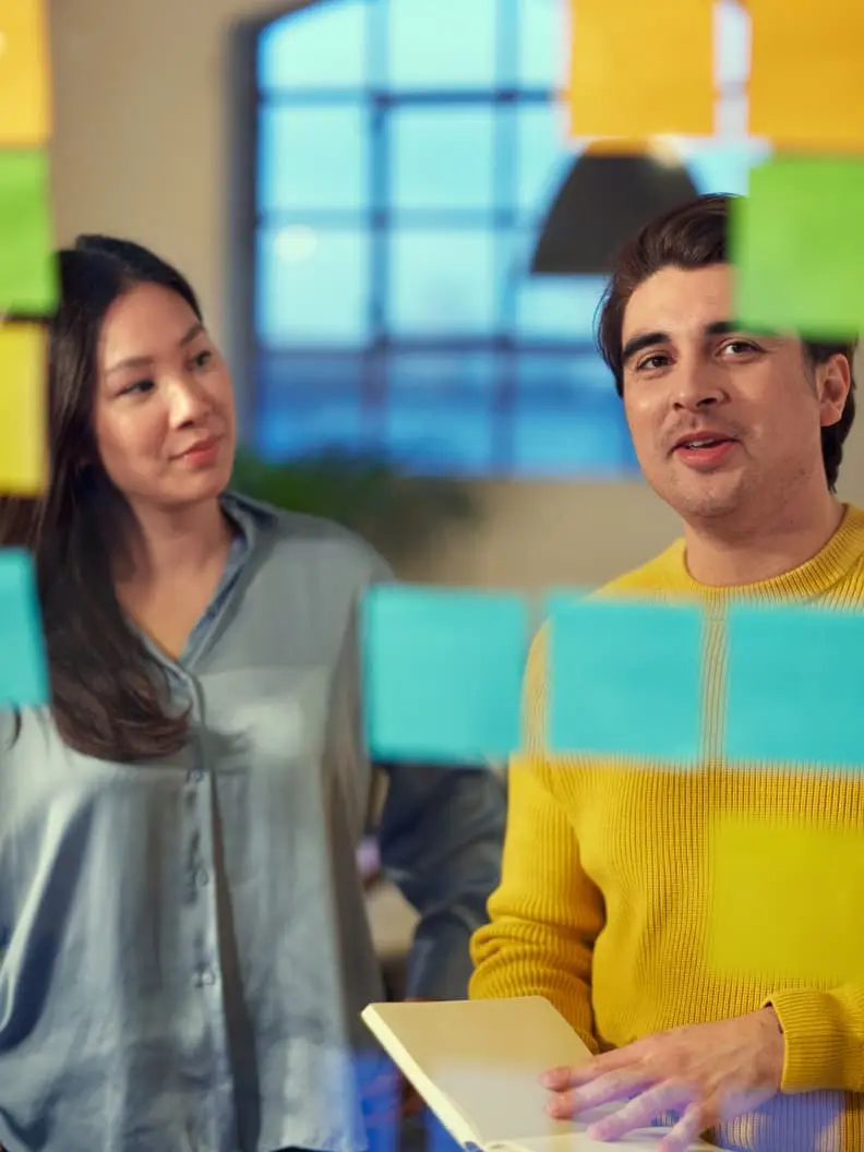 Two colleagues discussing work with sticky notes in the background.