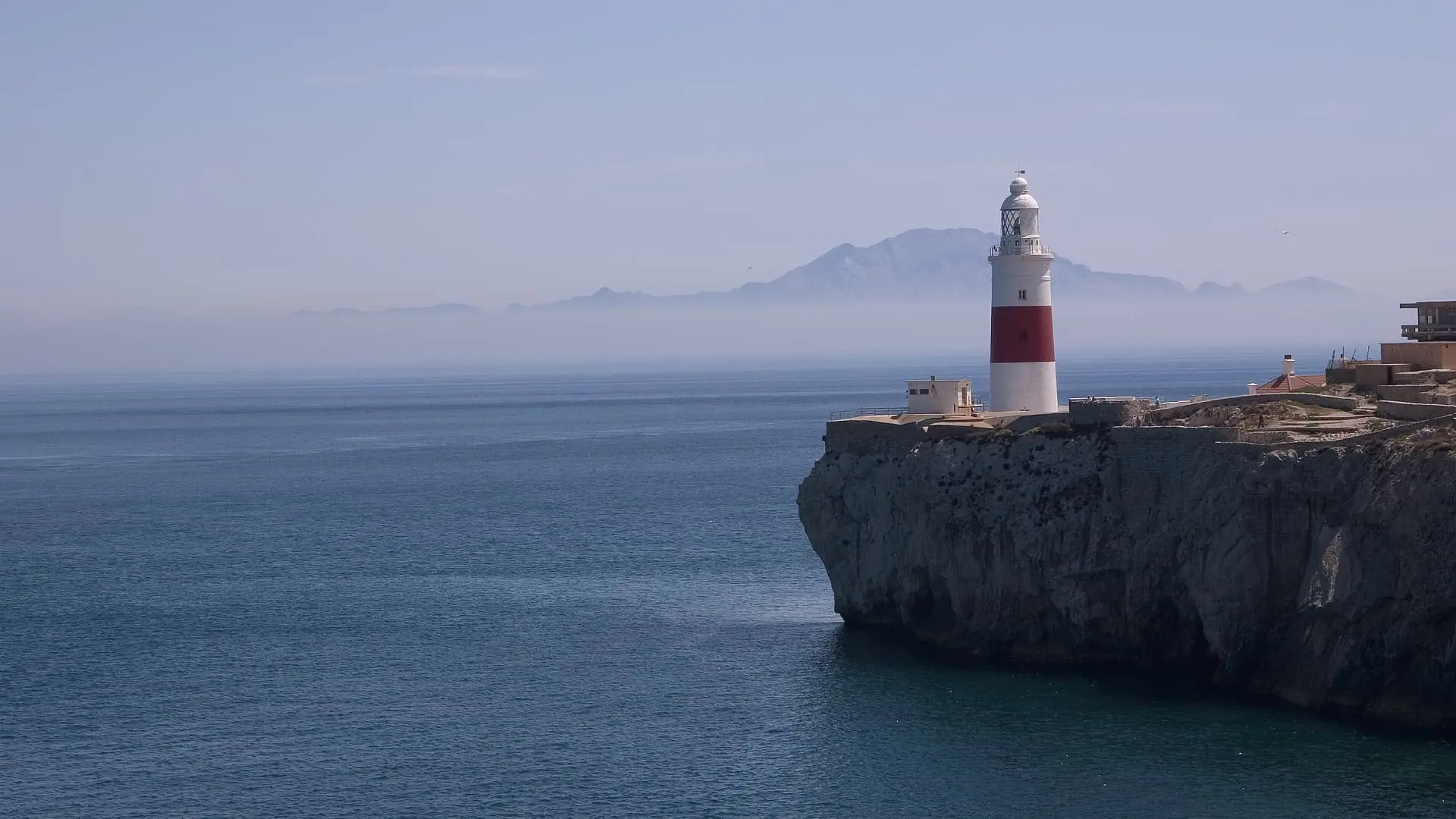 Lighthouse on a cliff overlooking a calm sea with distant mountains in haze in Gibraltar.