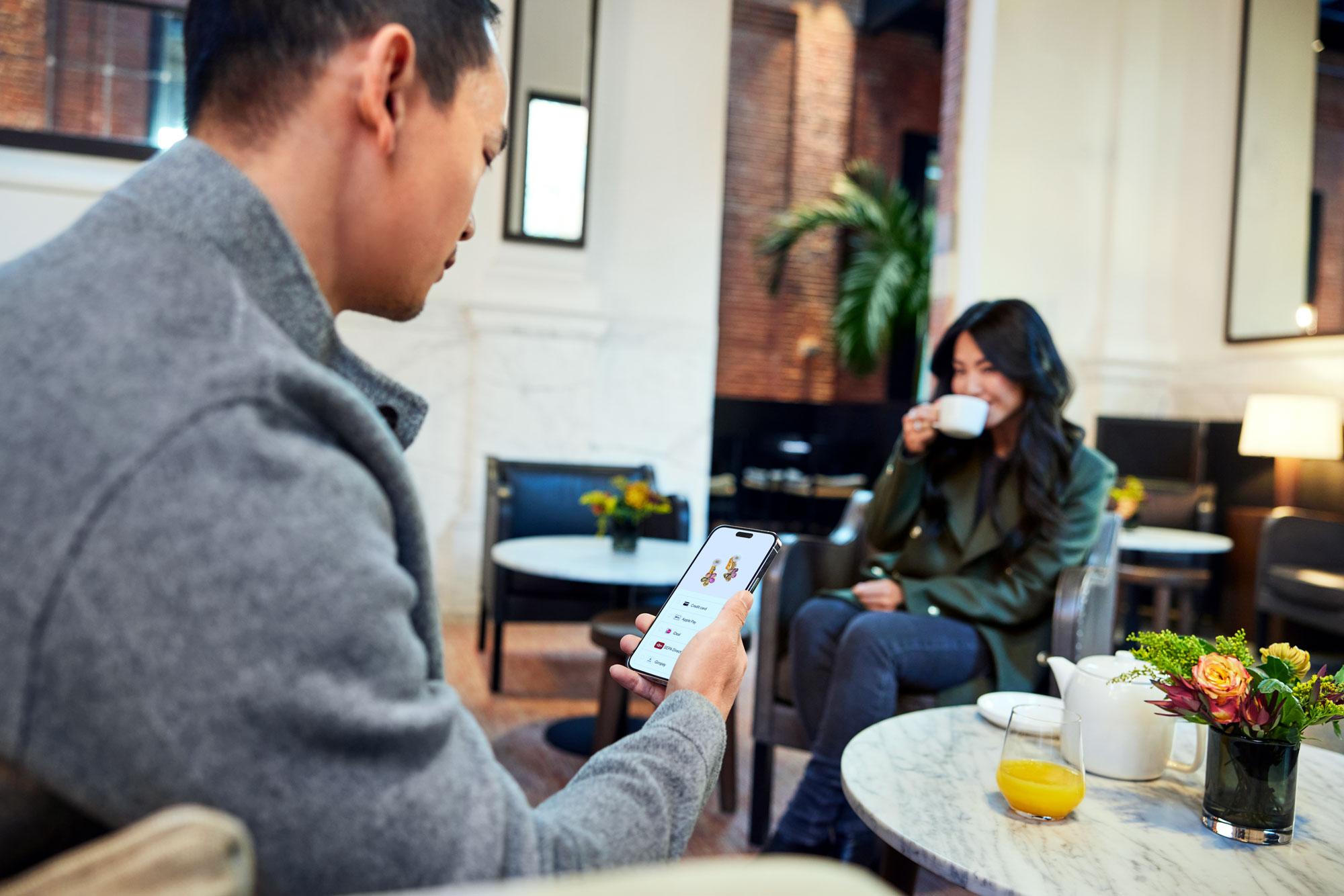 A couple sitting in a cafe and shopping for jewelry on a phone.