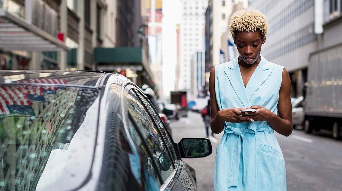 Woman in a blue dress using her smartphone on a city street.
