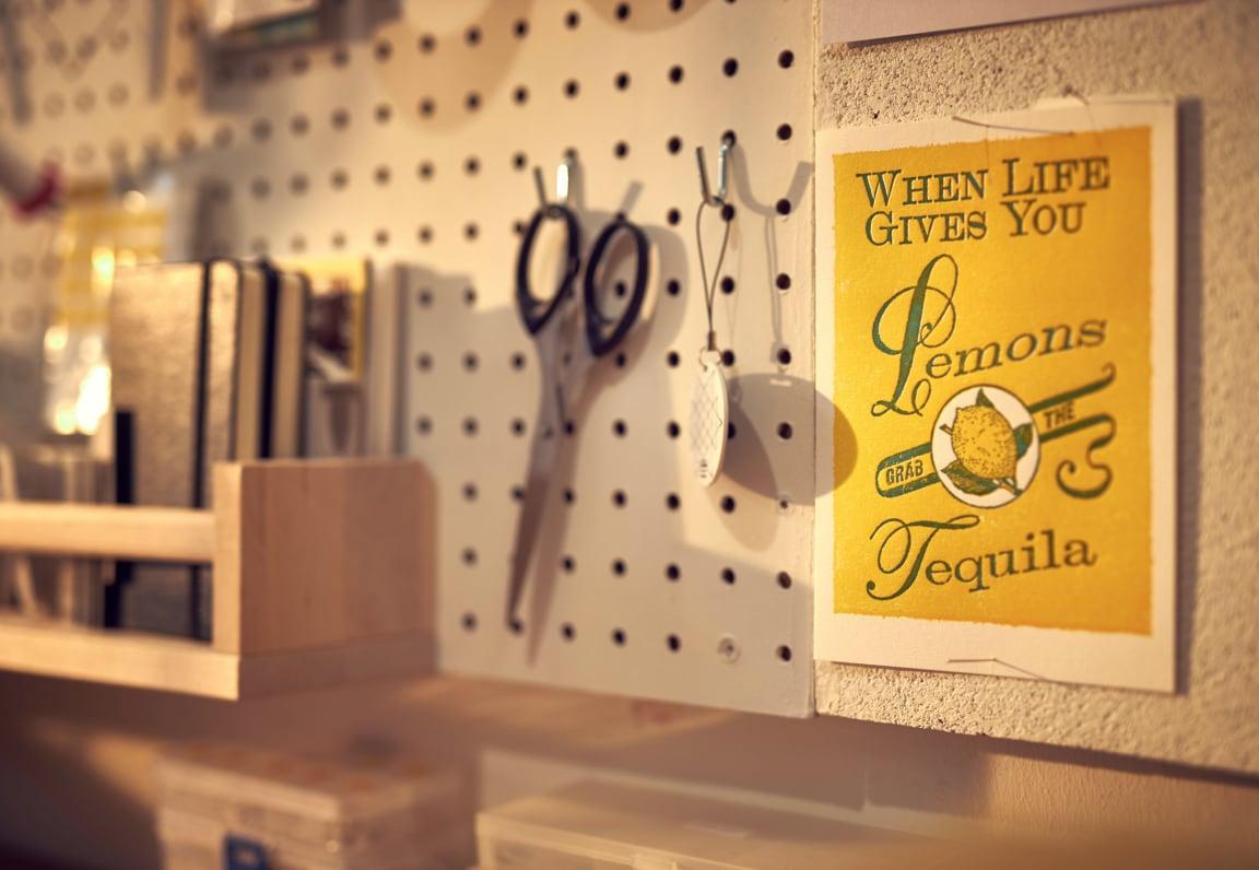 Schere hängend an einem Pegboard neben einem humorvollen Tequila-Zitat-Plakat.