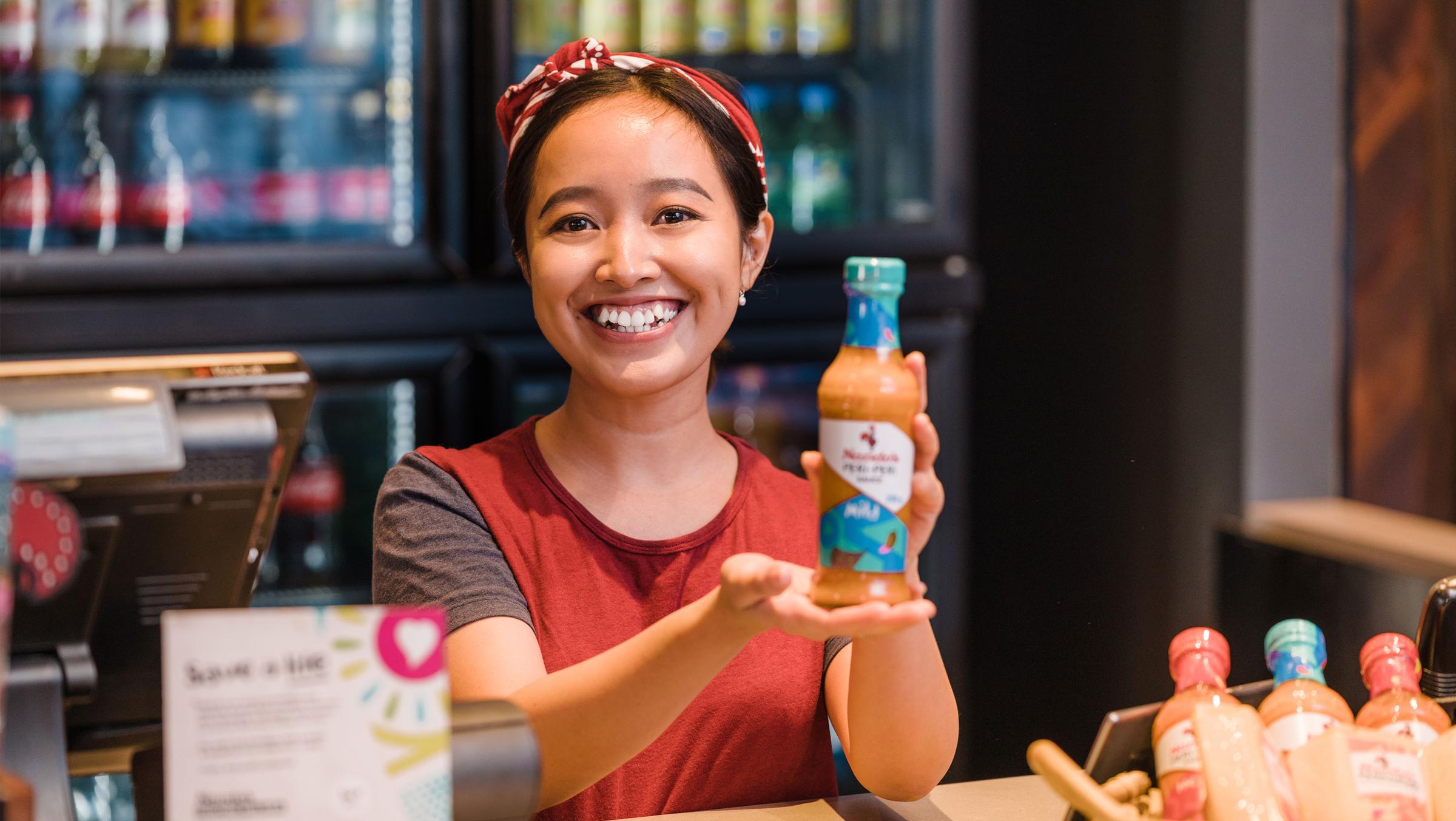Smiling woman presenting a bottle of sauce in a cafe.