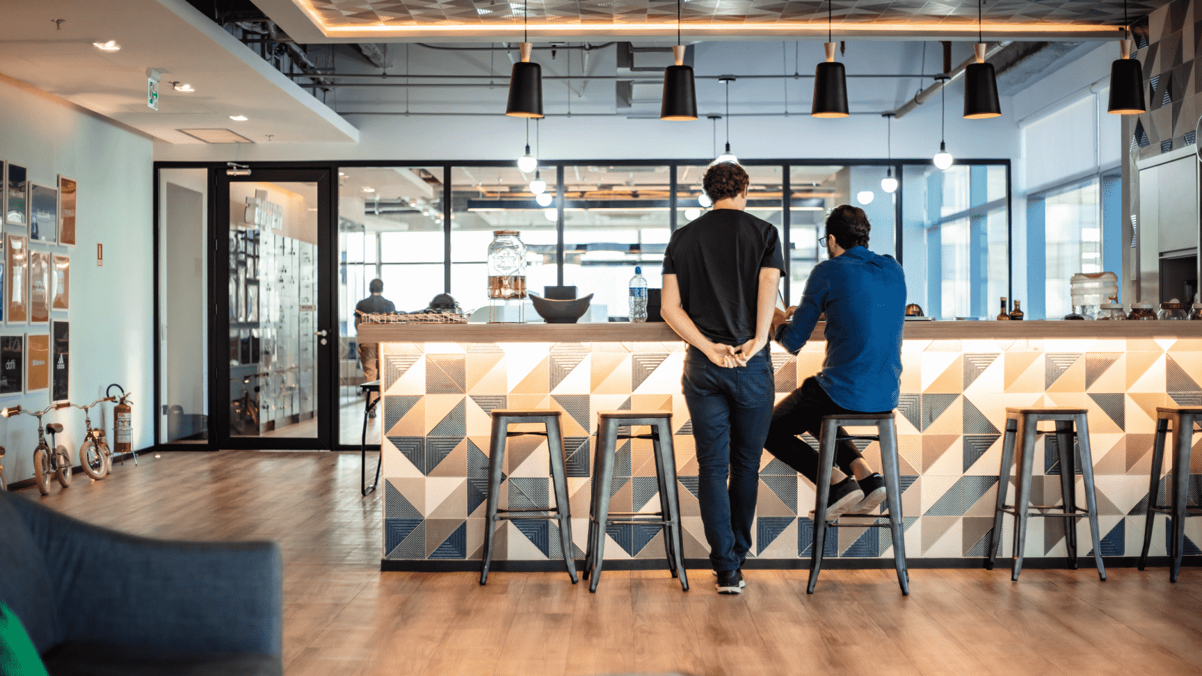 Duas pessoas sentadas em um balcão de bar moderno em uma cafeteria de escritório bem iluminada.