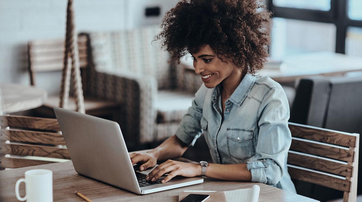 Smiling woman working on her laptop at a wooden table.