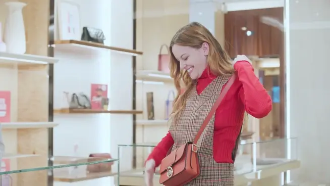 Mujer sonriendo con un suéter rojo mirando su bolso mientras compra en la tienda Longchamp.