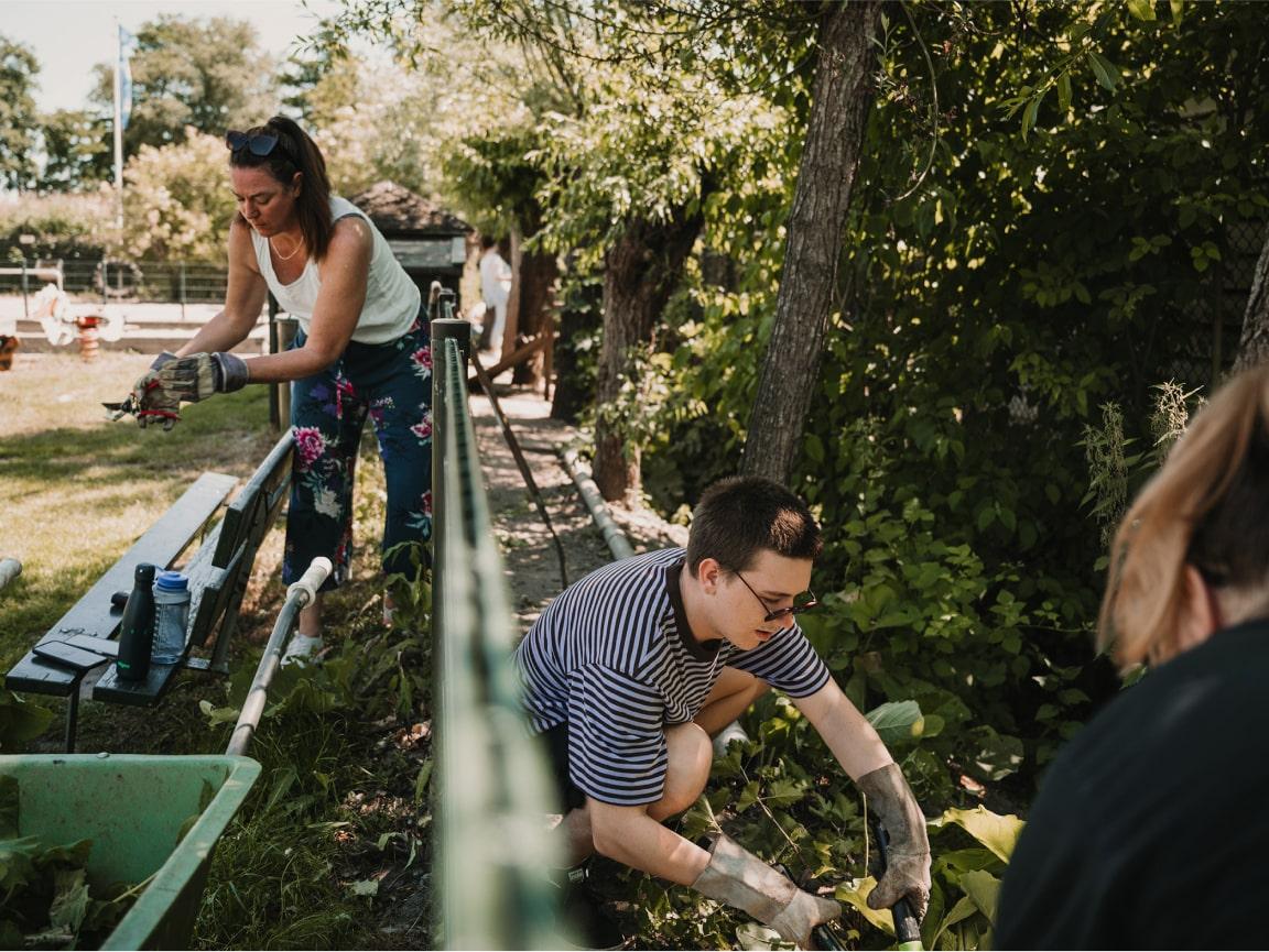 Two people gardening, one standing and cleaning, the other kneeling and digging.