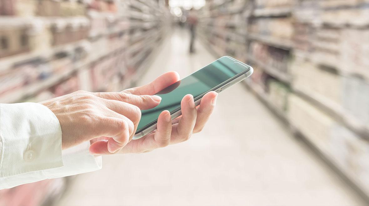 Primer plano de una mano sosteniendo un smartphone en un pasillo de supermercado.
