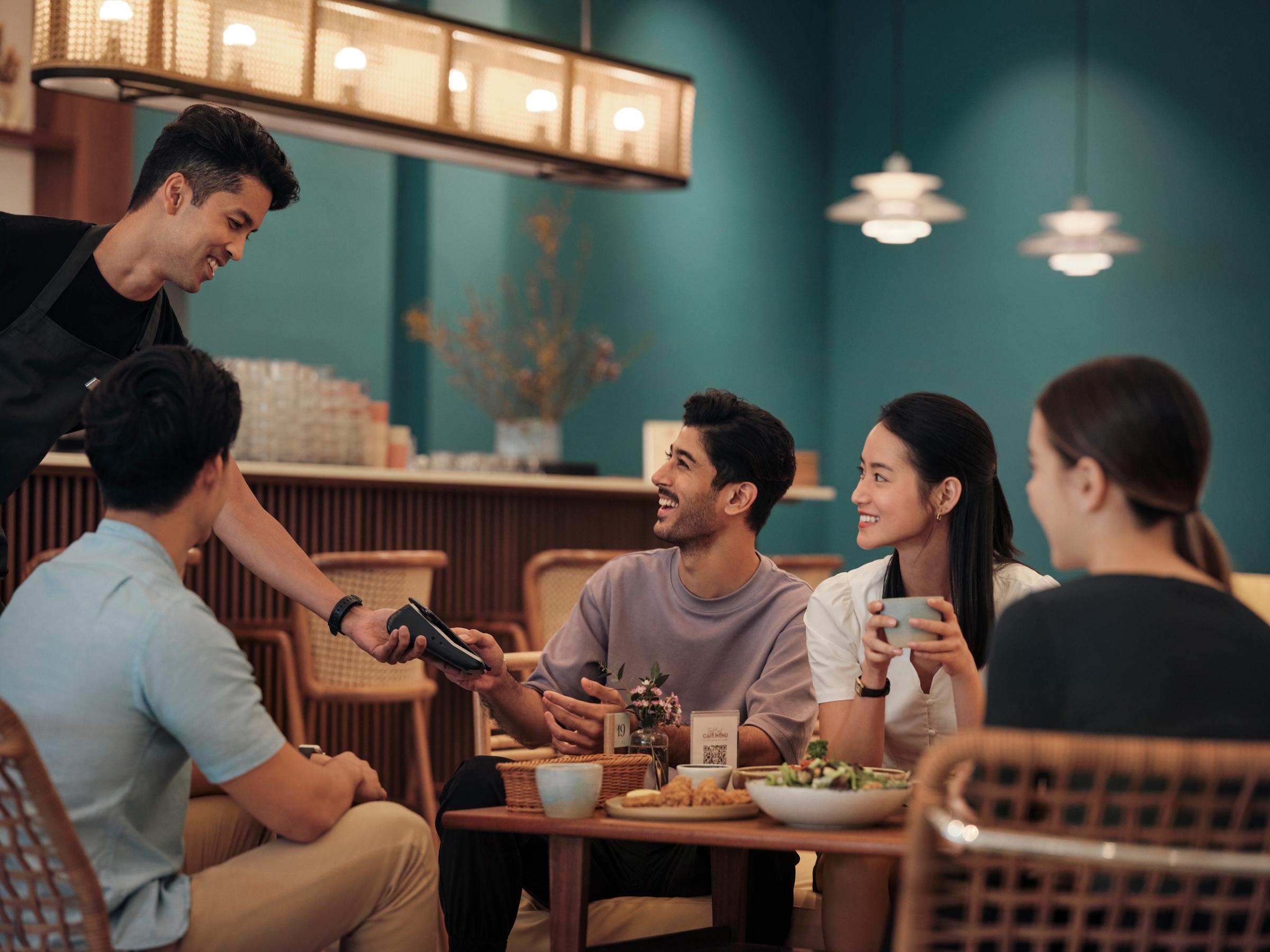 A man at a restaurant counter, paying for his order by tapping his phone on Adyen’s V400m terminal.