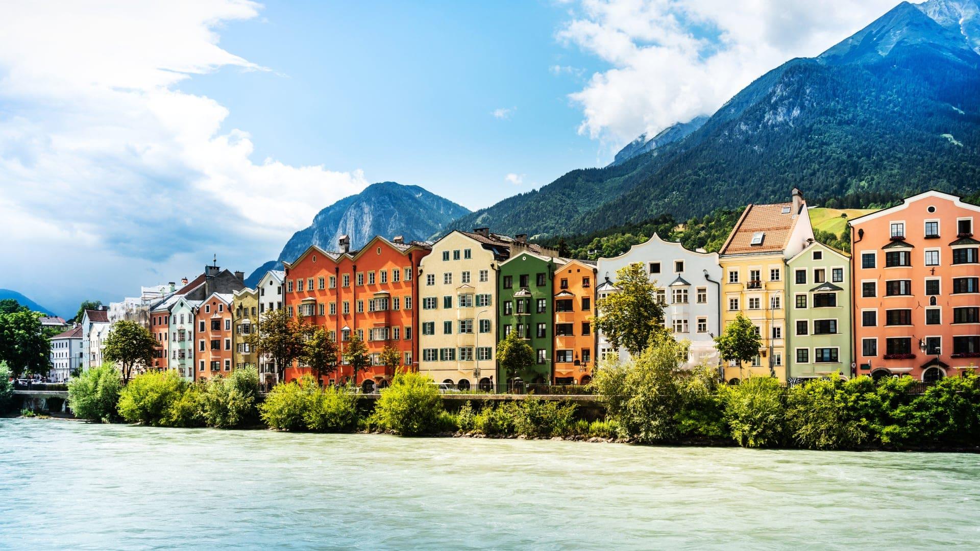 Bunte Gebäude entlang eines Flusses mit Bergen im Hintergrund in Österreich