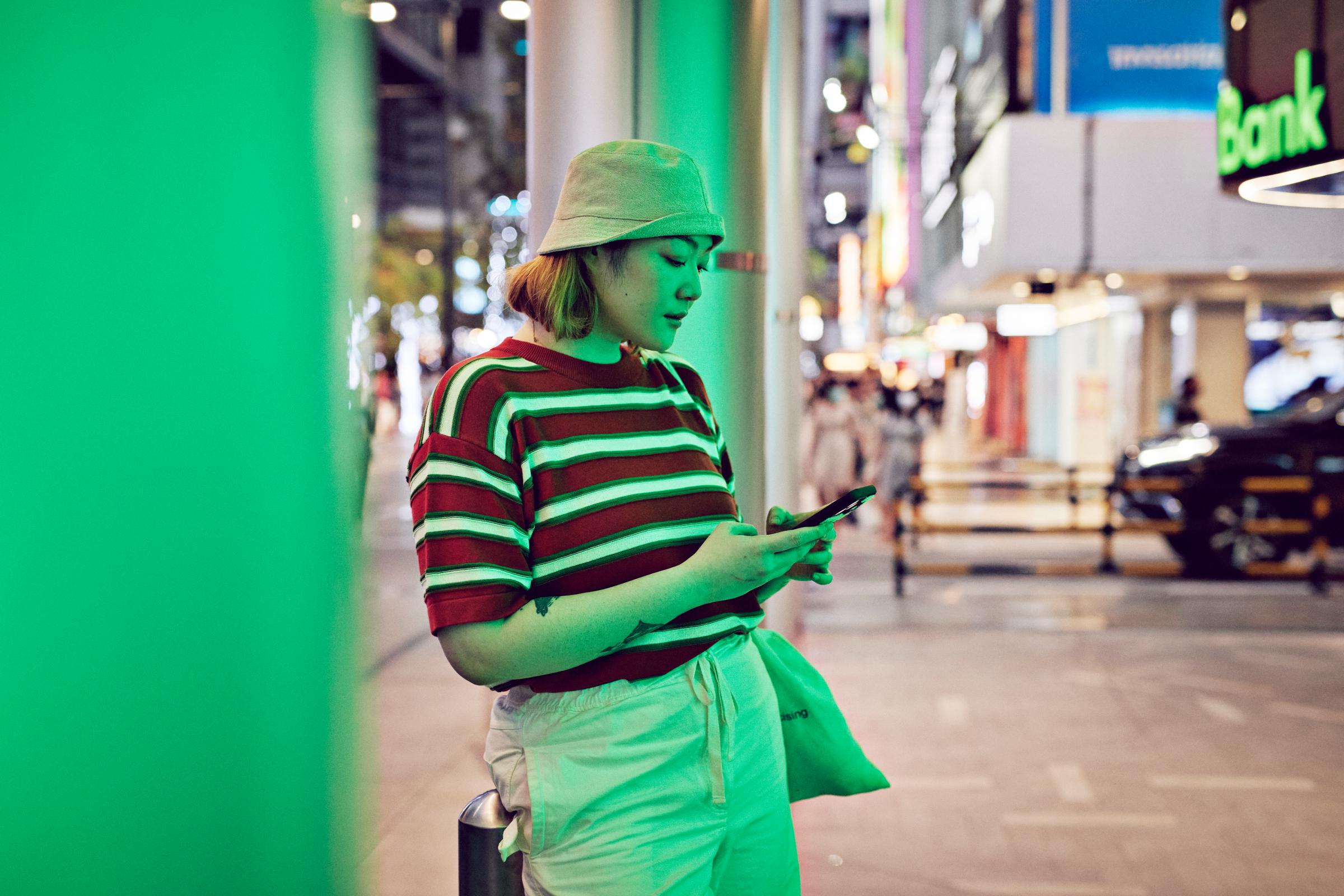 A person using a mobile device in an urban shopping district at night.