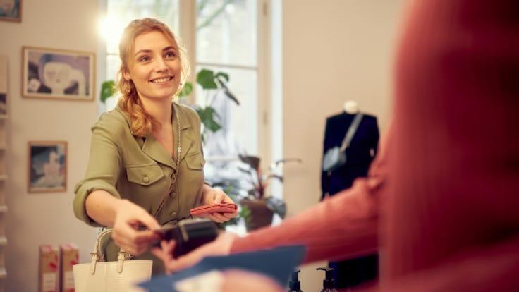 Cajera sonriente entregando un lector de tarjetas para pago en una boutique.