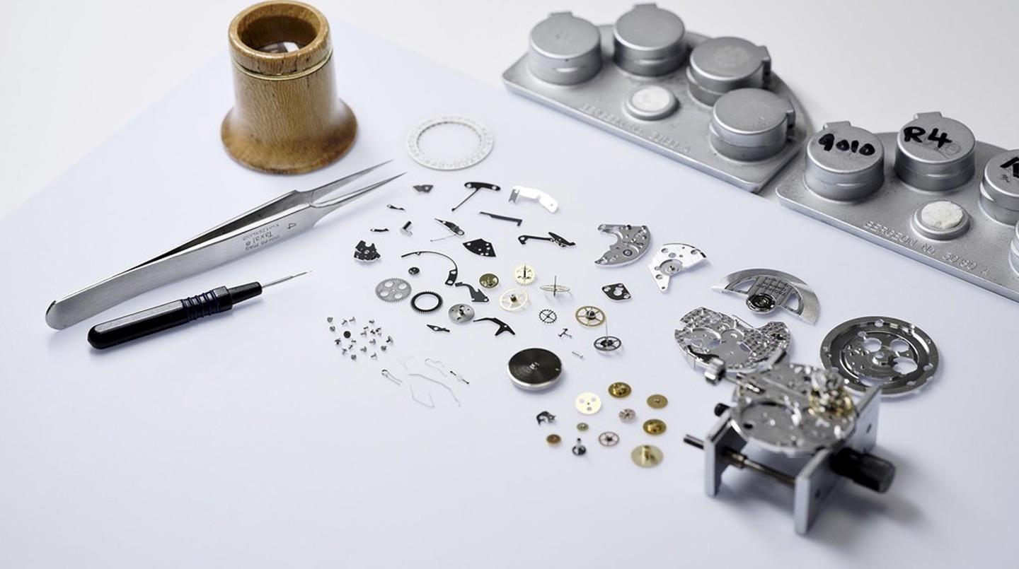 Parti di orologi smontati sparse su un tavolo con strumenti per la riparazione degli orologi