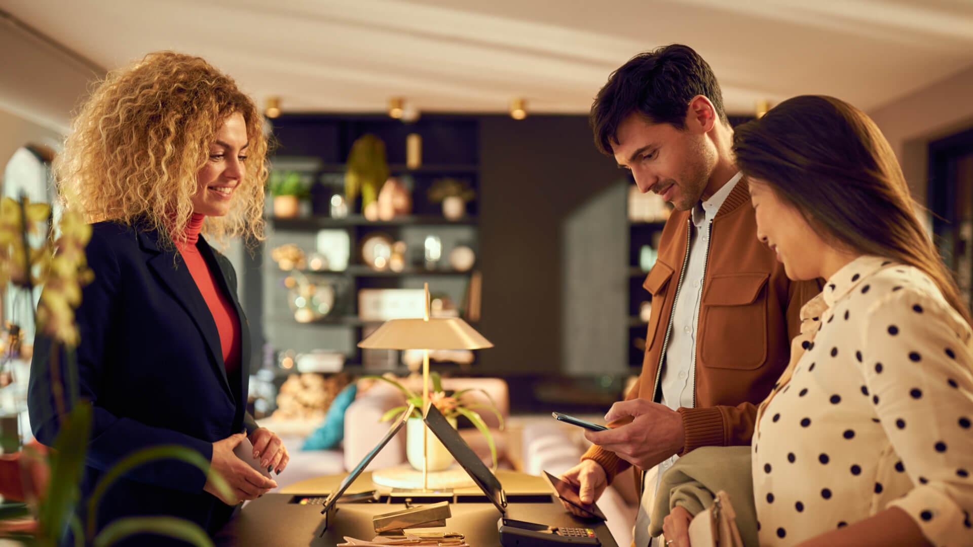 Três pessoas no caixa de uma loja, um funcionário e dois clientes, com uma transação por smartphone