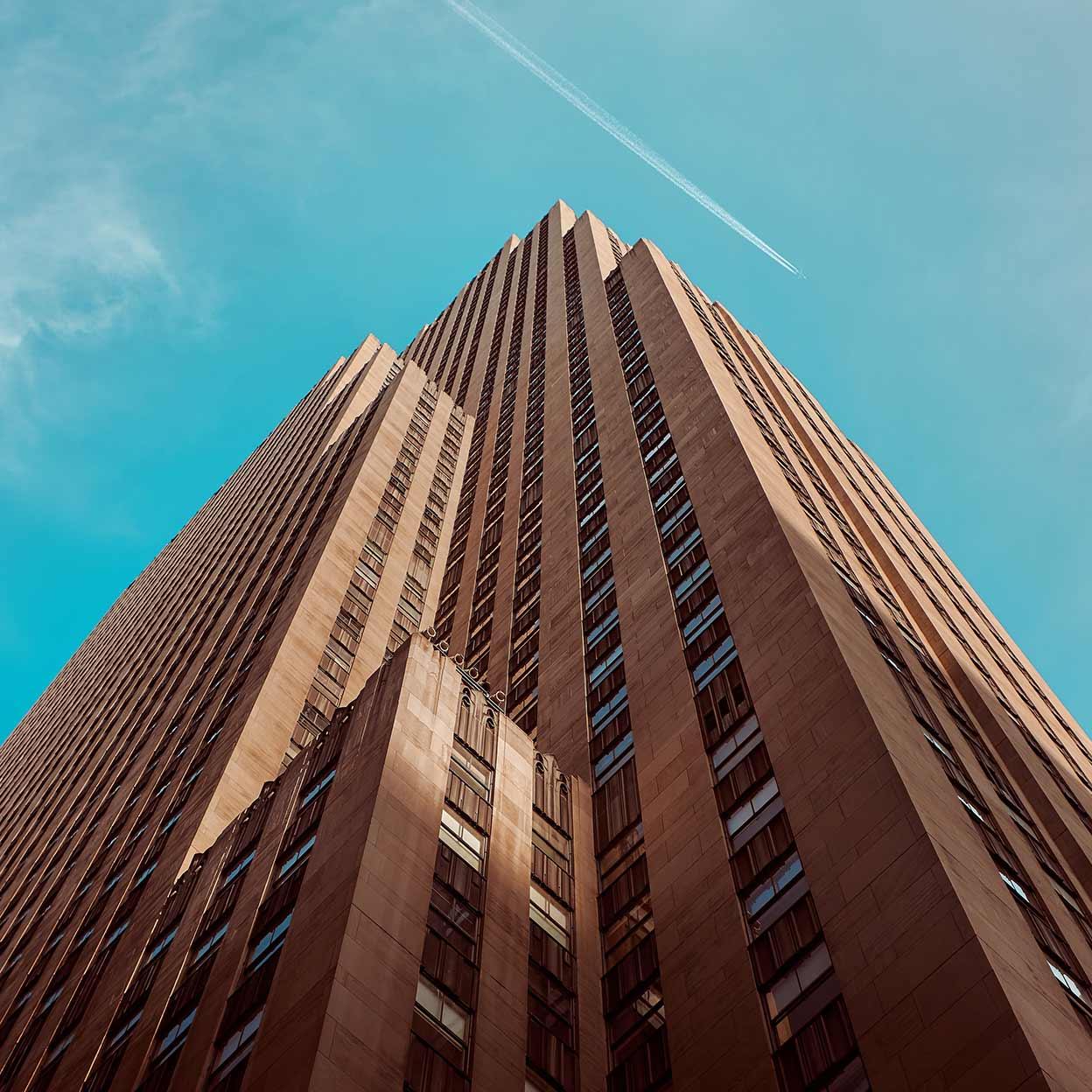 Ser på et høyt skyskraper mot en klar blå himmel med et fly som flyr over