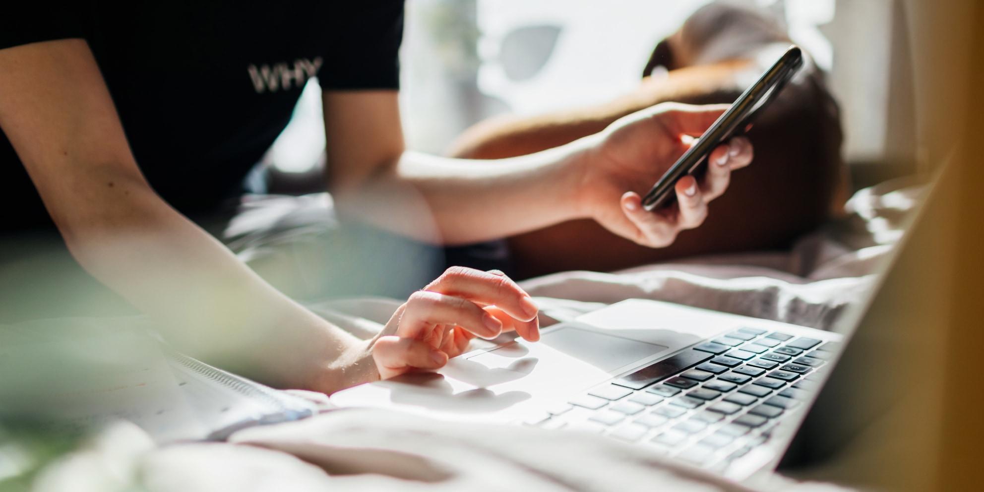 Person lying down using a smartphone and a laptop simultaneously.