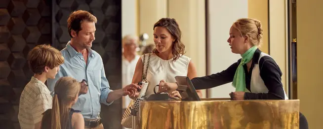 Family checking in at hotel reception, employee processing payment with Adyen terminal.