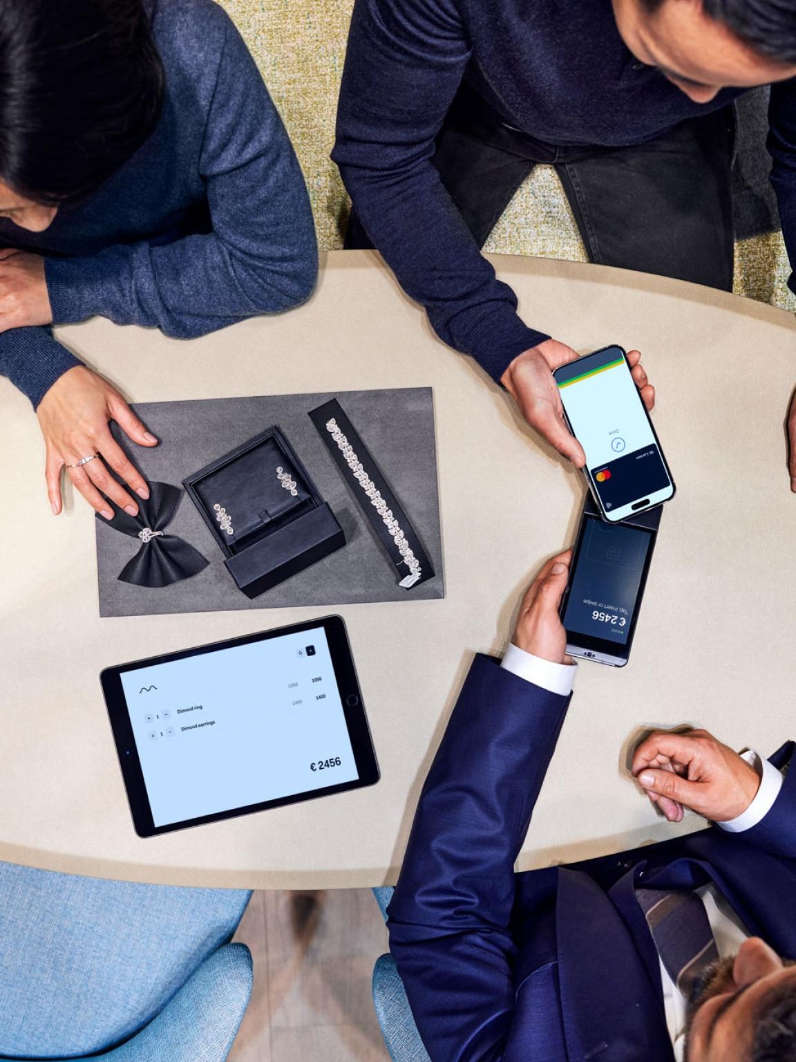 Tre persone intorno a un tavolo con dispositivi di pagamento Adyen tra cui uno smartphone e un tablet che visualizzano transazioni.