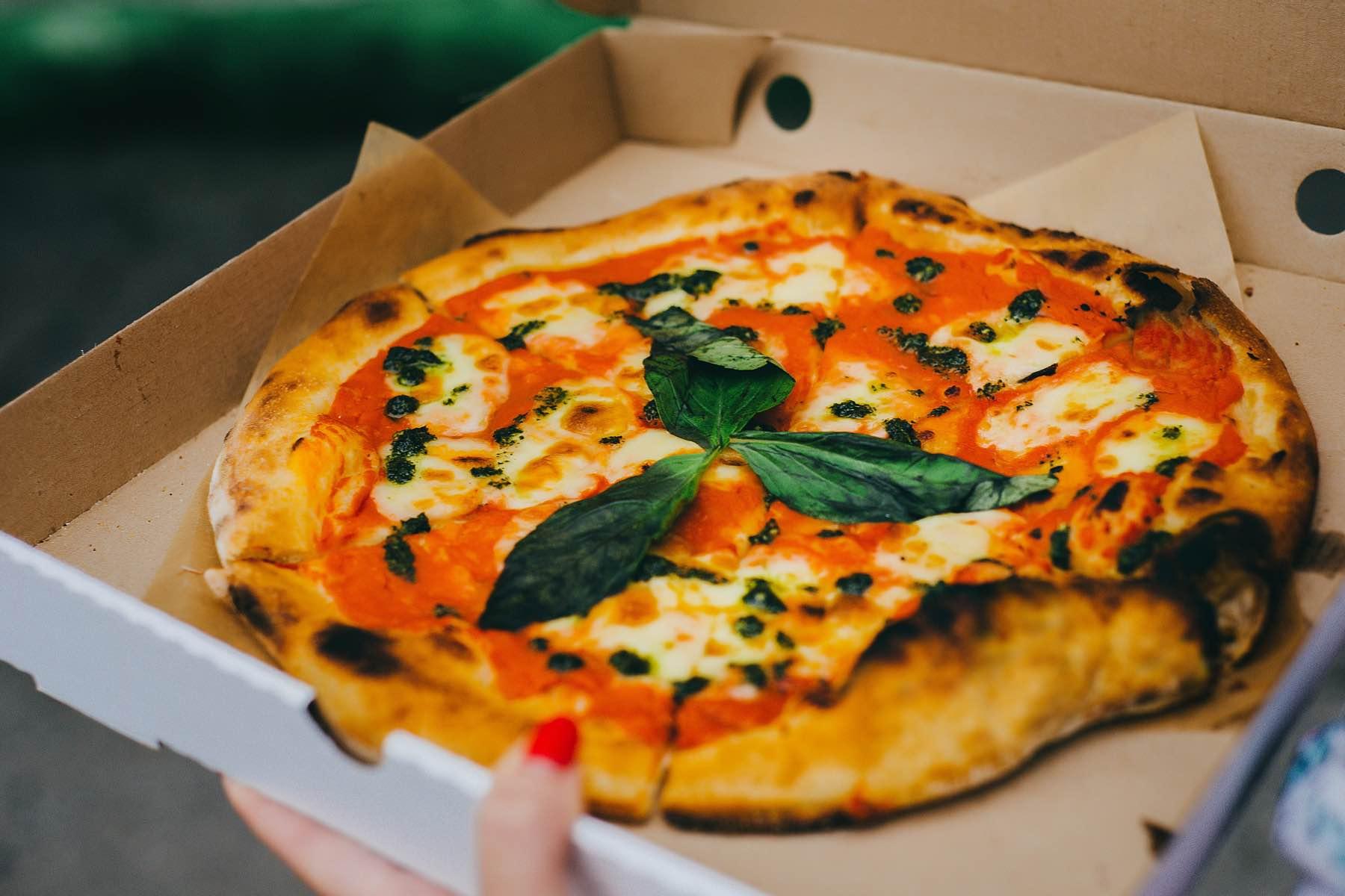 Freshly baked pizza with melted cheese and basil leaves in a cardboard box.