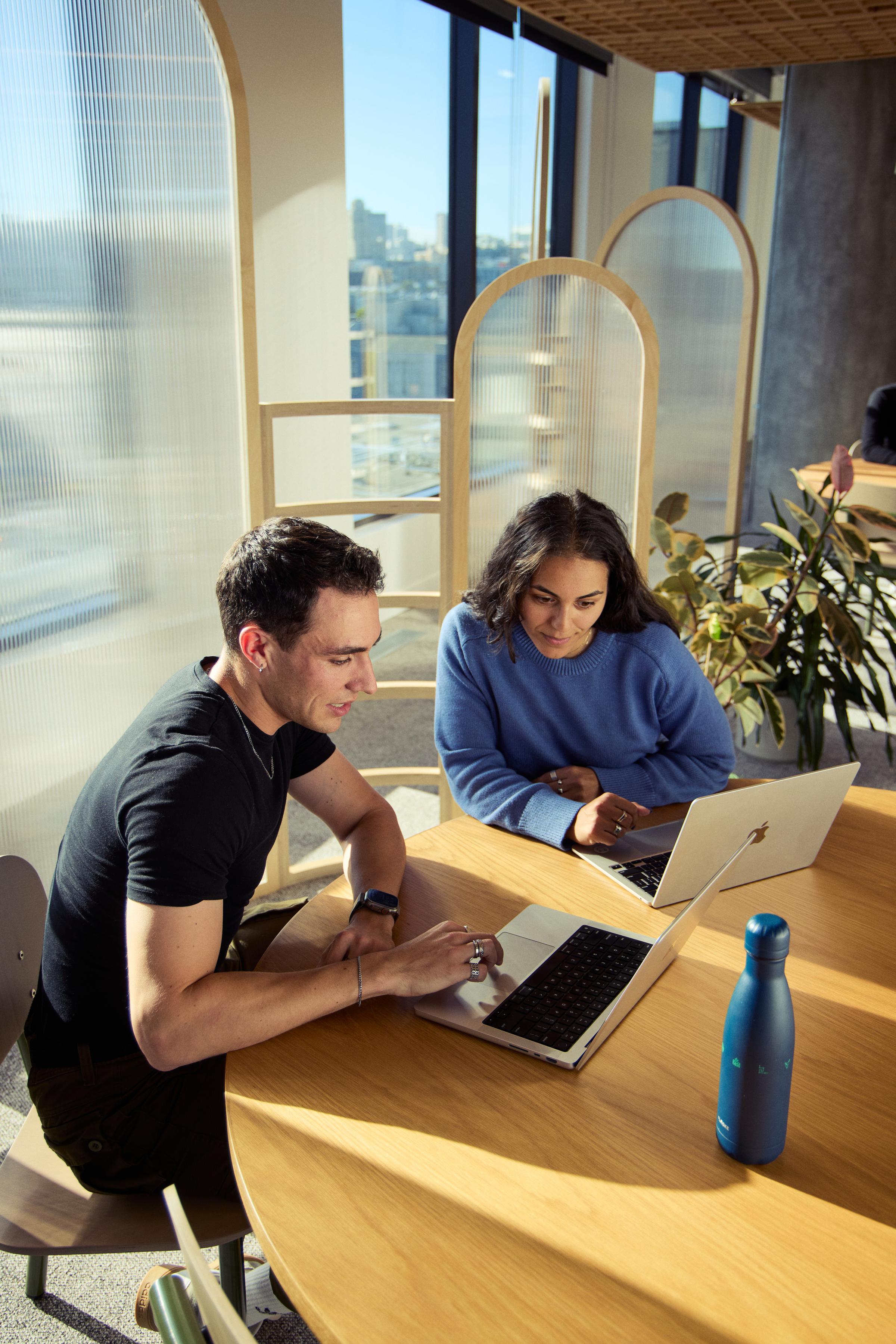 Two employees collaborating with laptops at a shared work table