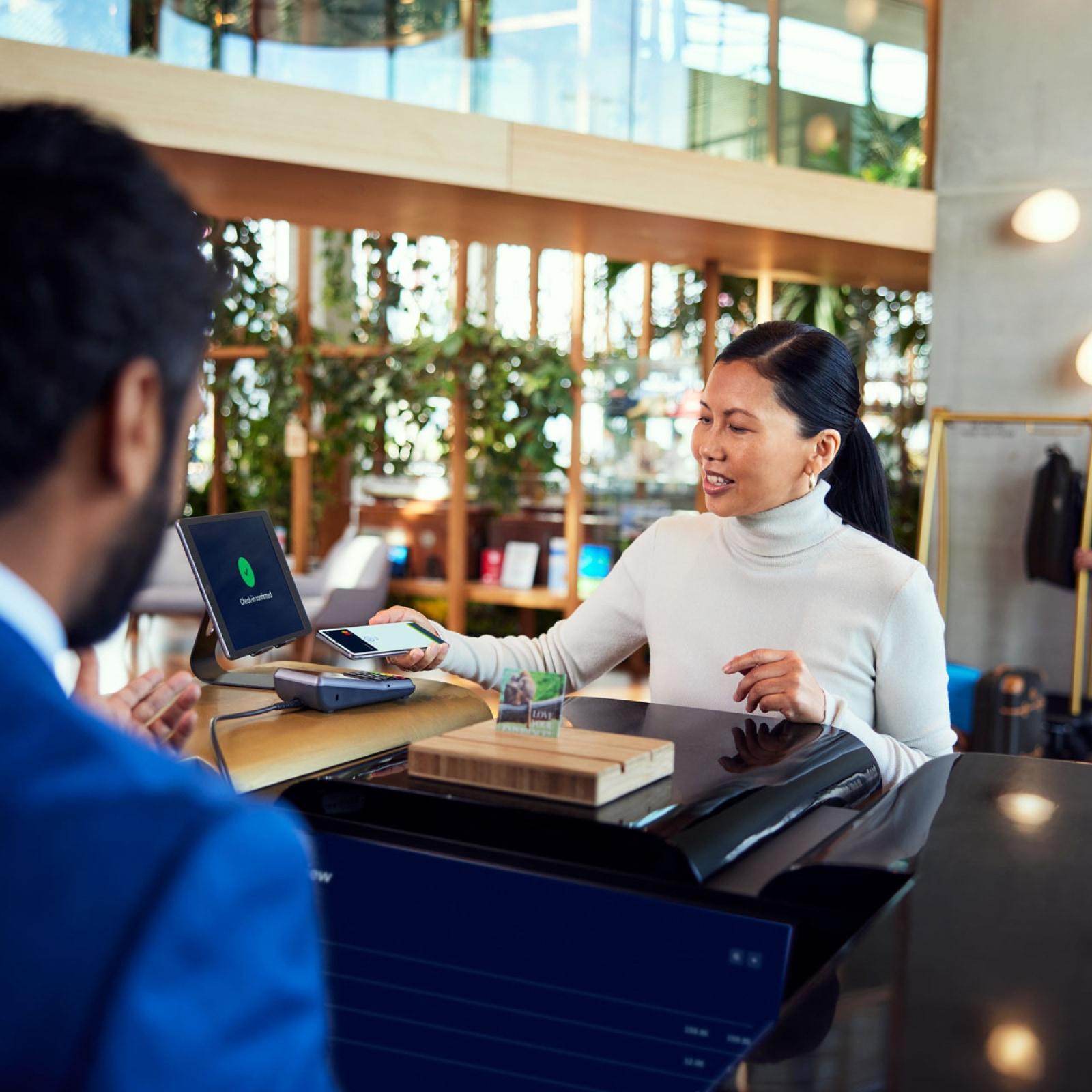 Two people at a checkout counter with a customer using a mobile phone to make a contactless payment on an Adyen terminal.