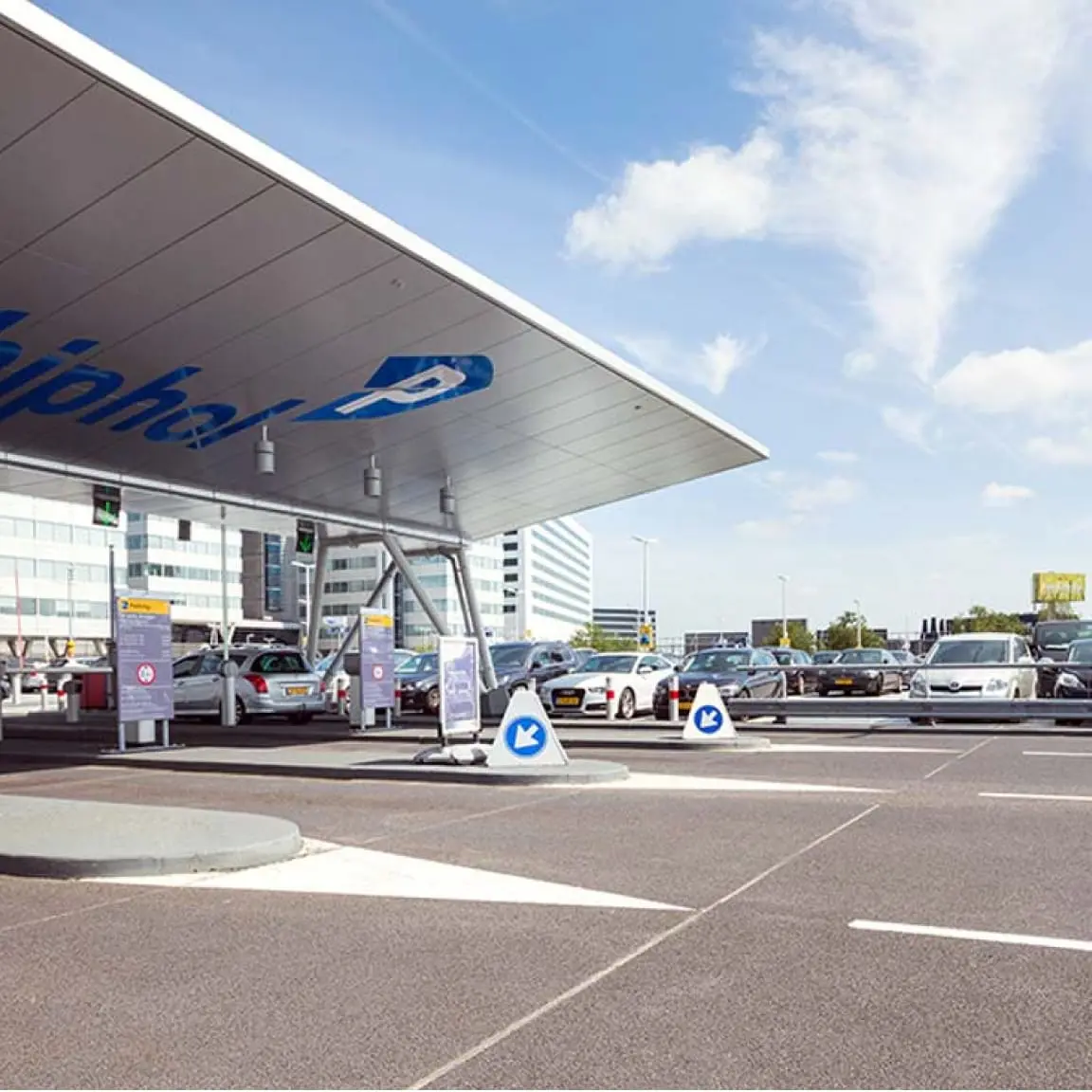 Vehículos entrando y saliendo de un área de peaje de estacionamiento bajo un cielo despejado.