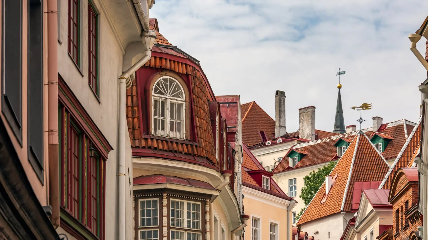 Historical building rooftops with dormer windows against a cloudy sky in Estonia.