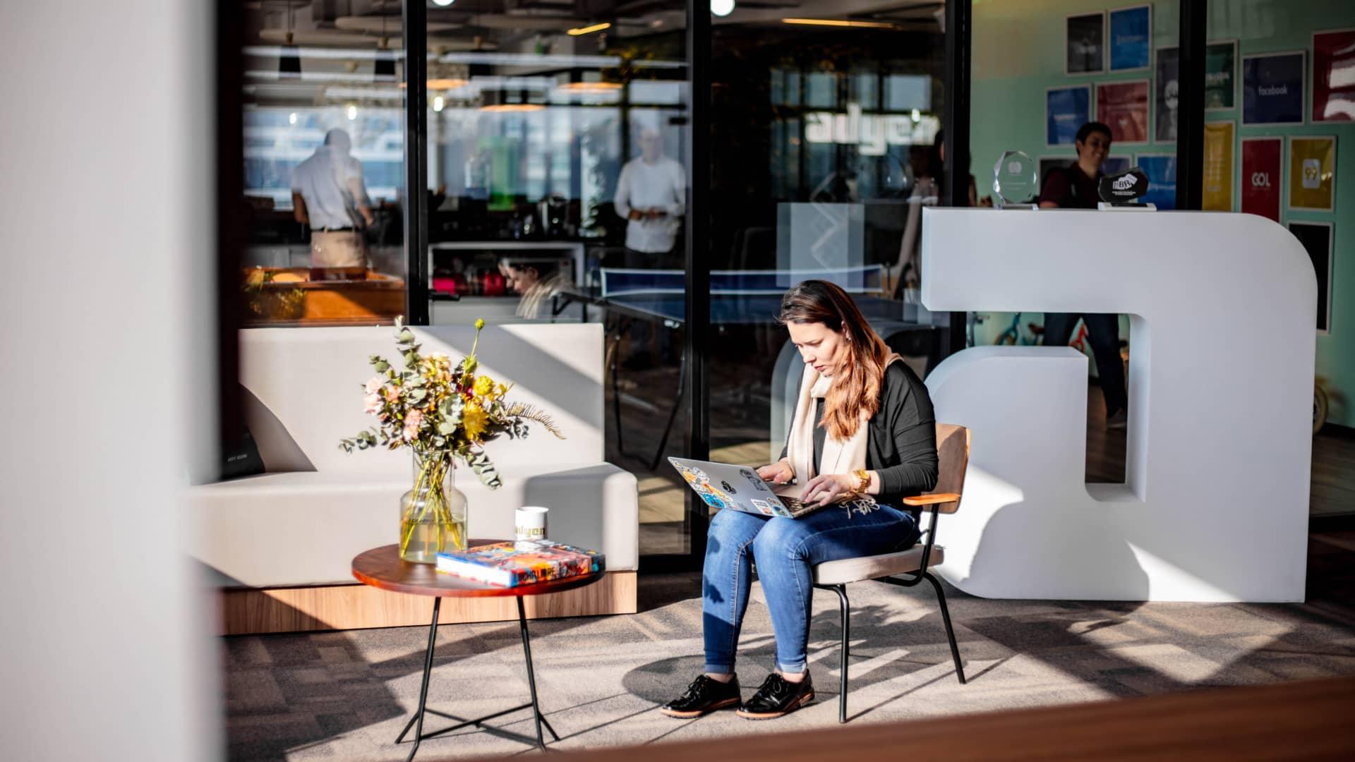 Pessoa sentada a uma mesa trabalhando em um laptop em um espaço de escritório moderno e iluminado.