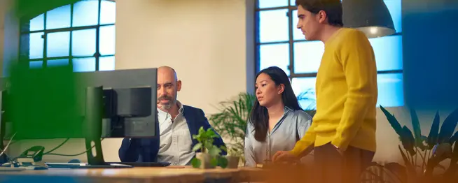 Drei Fachleute arbeiten an einem Computer in einem hellen Büroraum zusammen.
