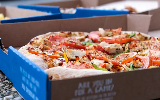 Close-up view of a fresh pizza with various toppings in a cardboard box.