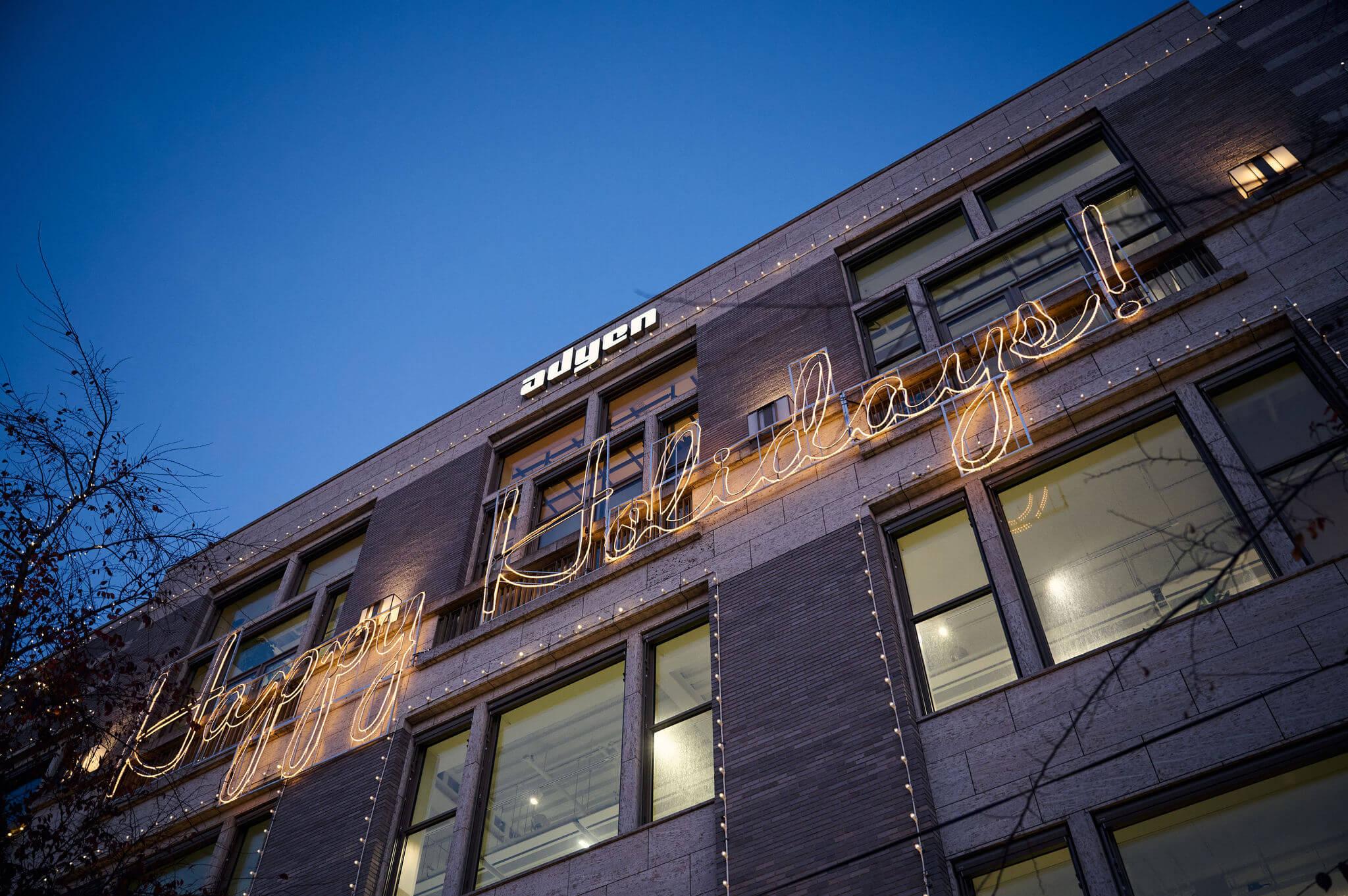 Office building adorned with 'Happy Holidays' lights and company signage.