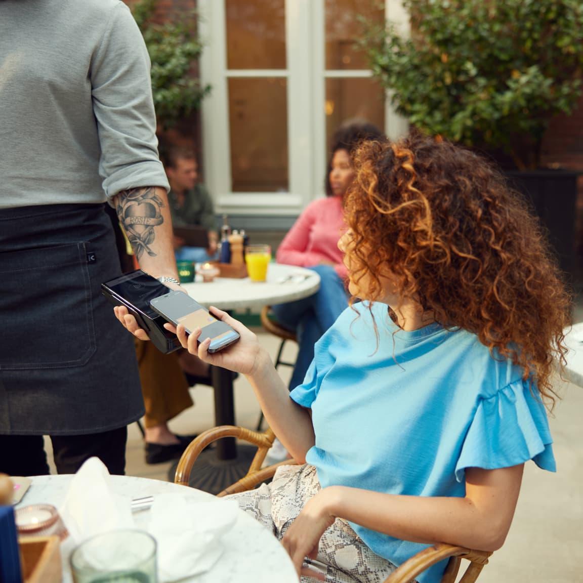 Woman using her phone to make a contactless payment to a server holding a card reader.