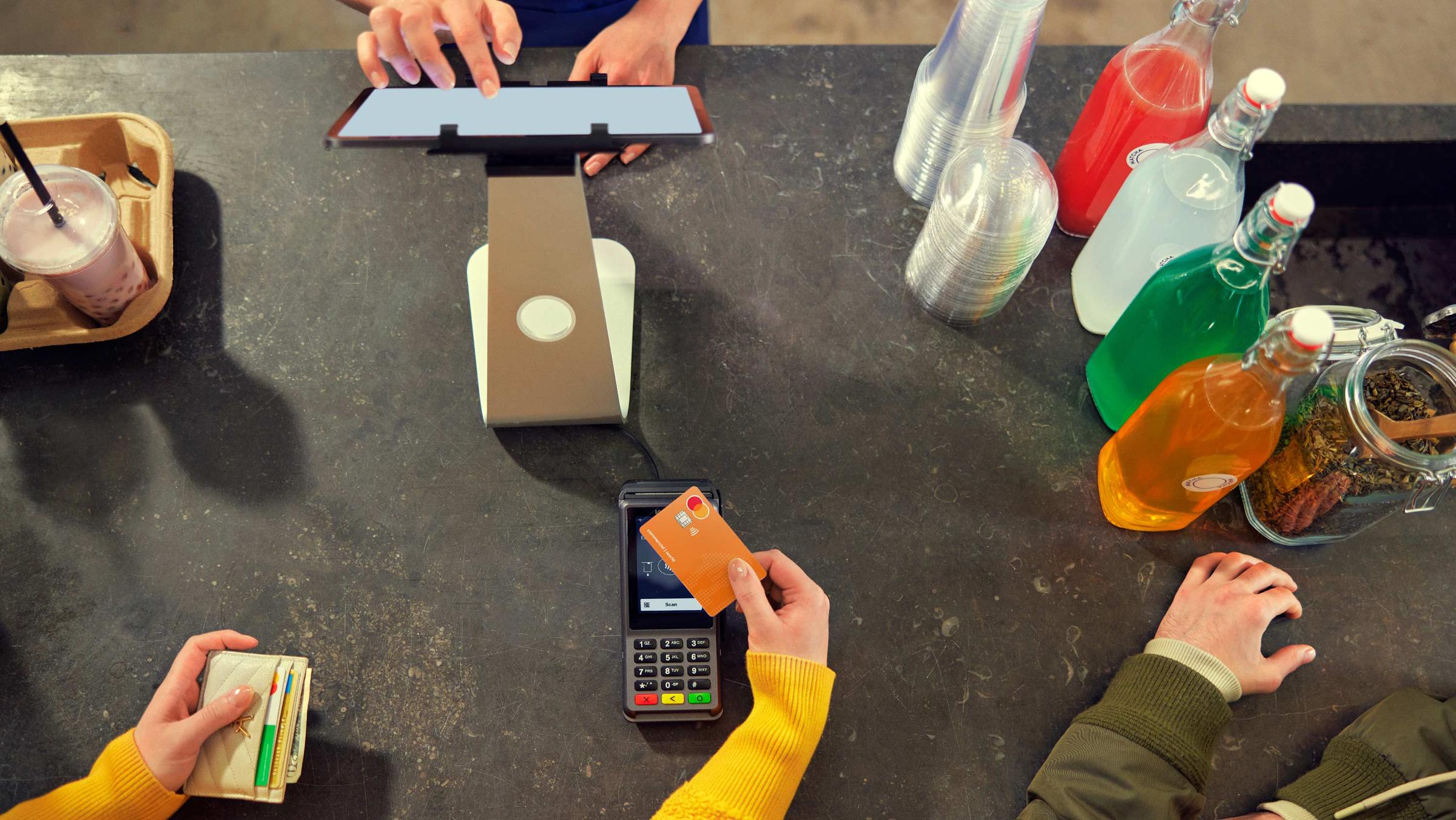 Person paying at a counter in a juicebar using an orange Mastercard card.