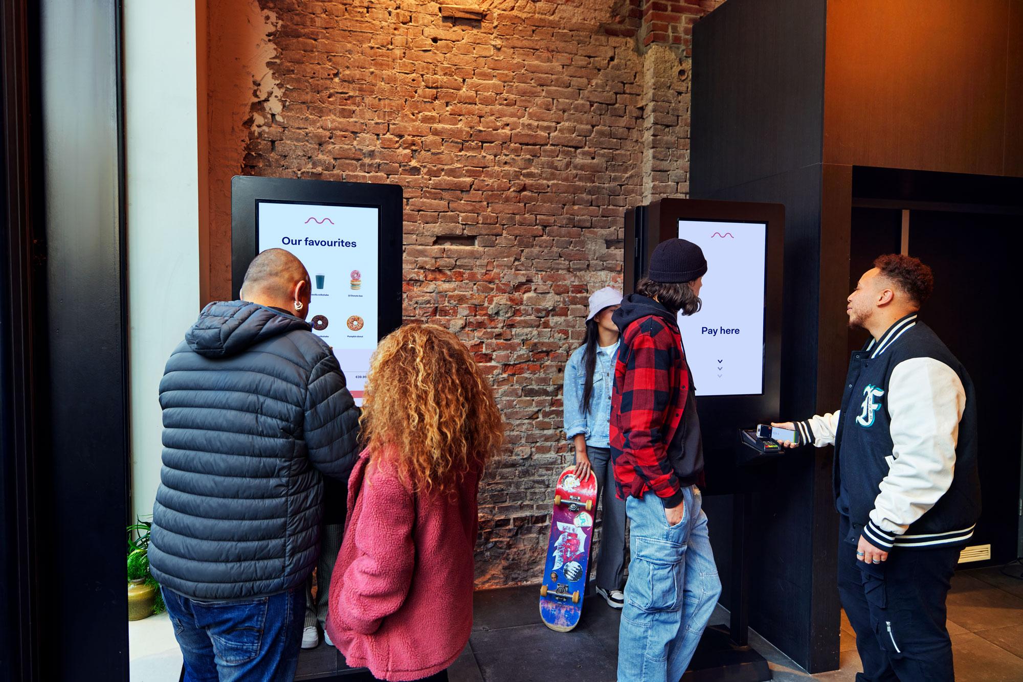 Customers at a donut shop placing an order using a kiosk with Adyen's terminal.