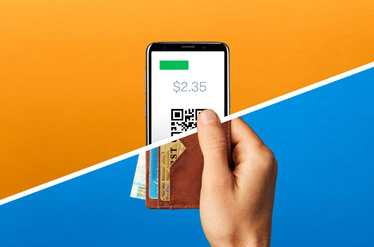Hand håller smartphone som visar QR-kod för betalning med sedlar i plånbok mot en splittrad orange och blå bakgrund.