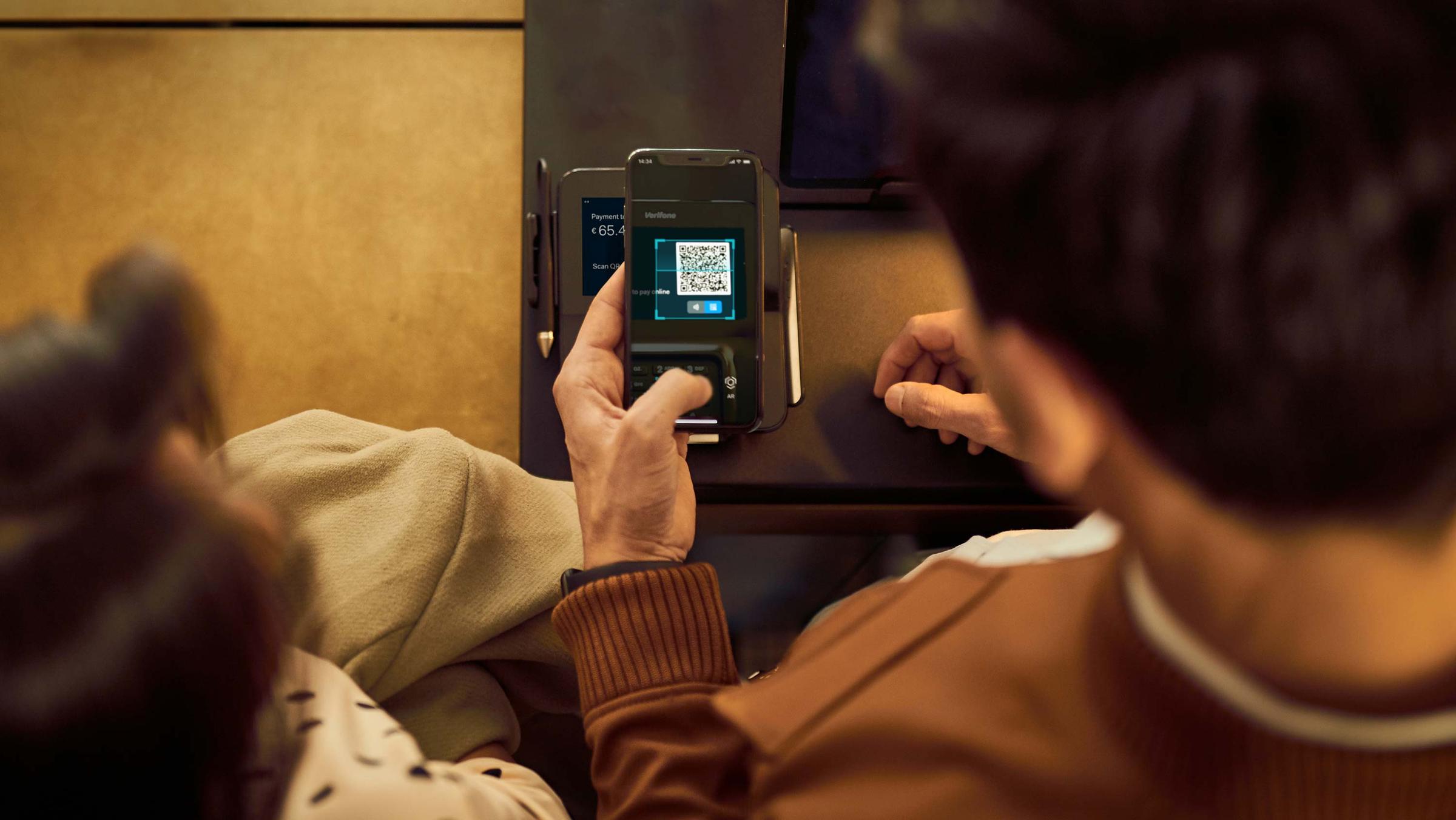 Person scanning QR code on a payment device screen for a transaction