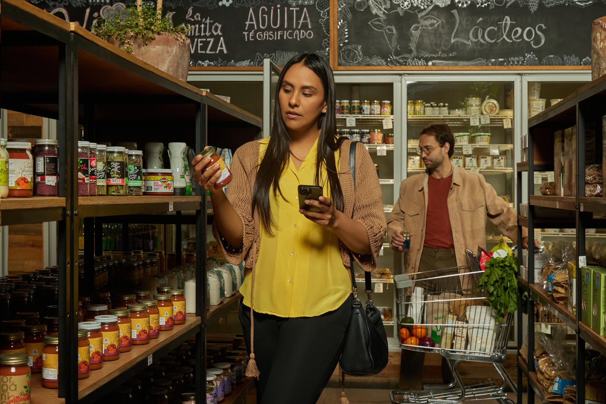 Una mujer con un teléfono móvil en una mano y un alimento enlatado en la otra