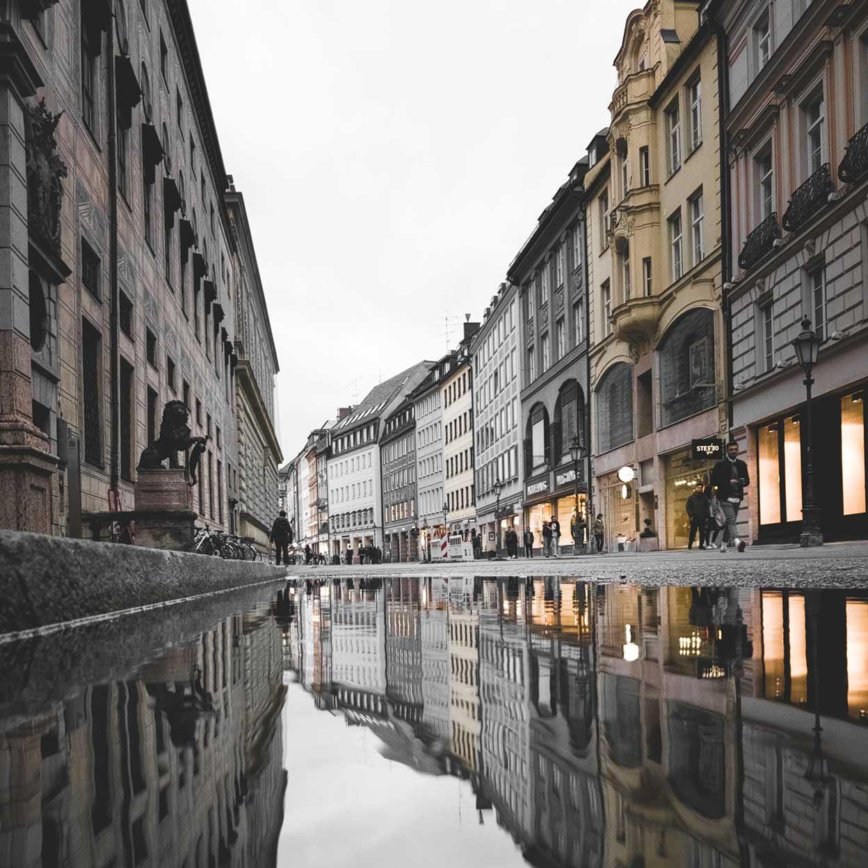 Refleksion af en bygade med bygninger og mennesker på en våd overflade